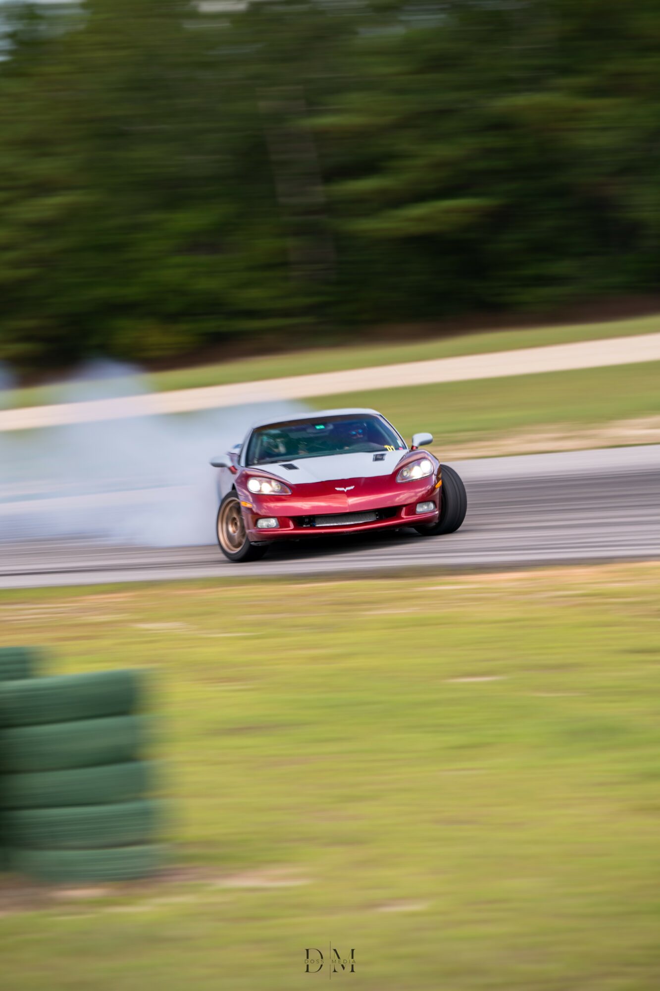 Red sports car drifting on a race track with smoke and blurred background of trees and grass.
