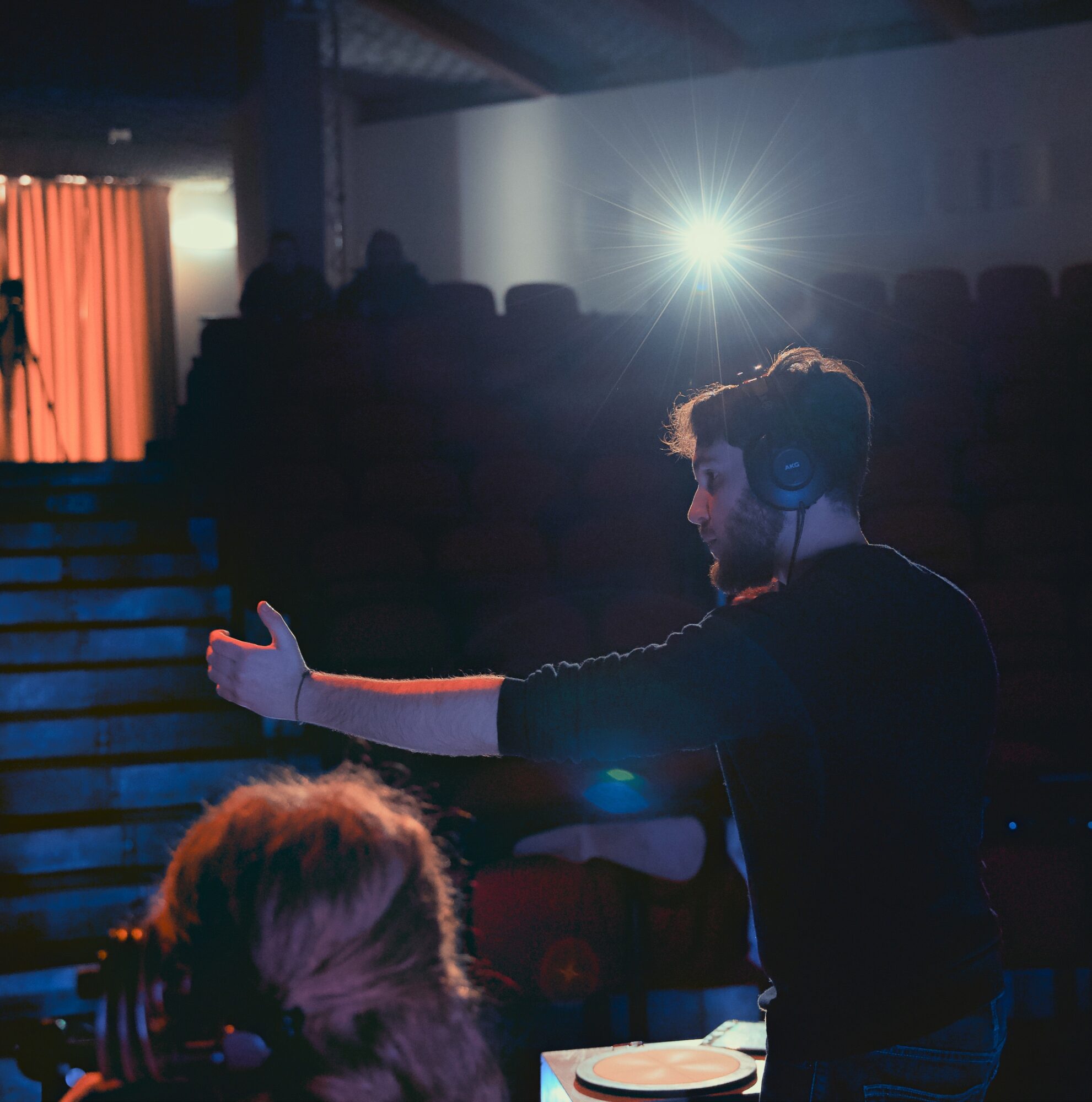 Person with headphones gesturing with arms extended in a dark room with stage lighting.