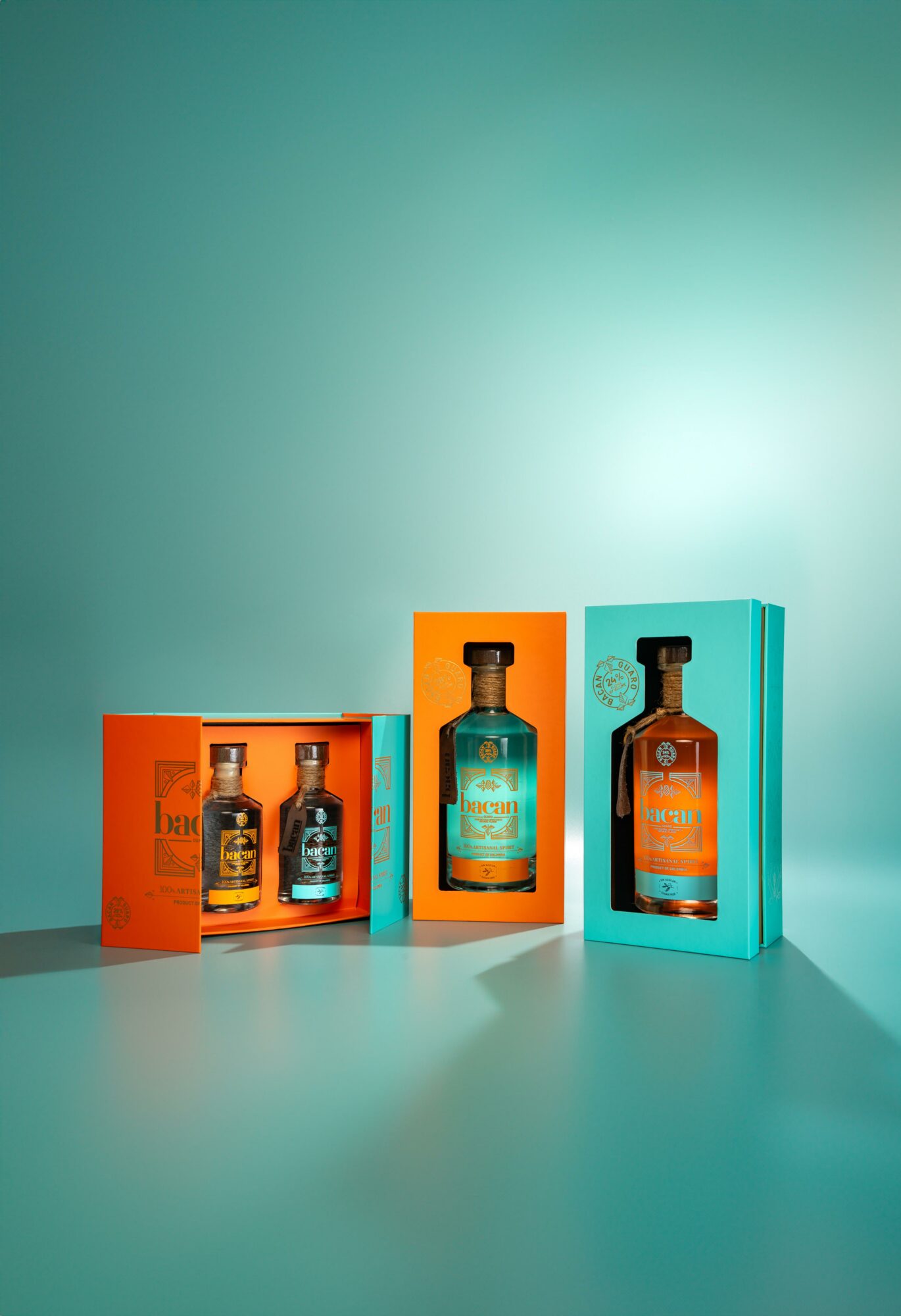 Three bottles of liquor in colorful boxes on a teal surface with a teal background.