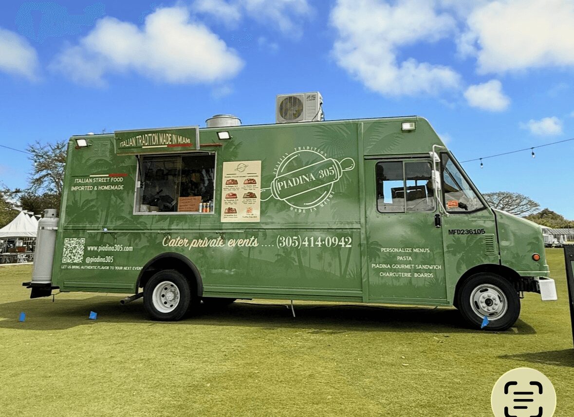 Green food truck parked on grass with blue sky and clouds, serving window open, menu visible.