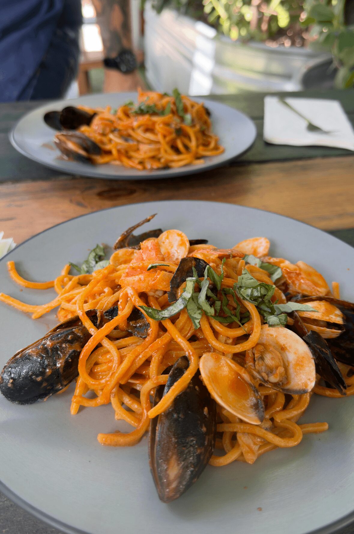 Plate of seafood pasta with mussels, shrimp, and green herbs on a wooden table outdoors.