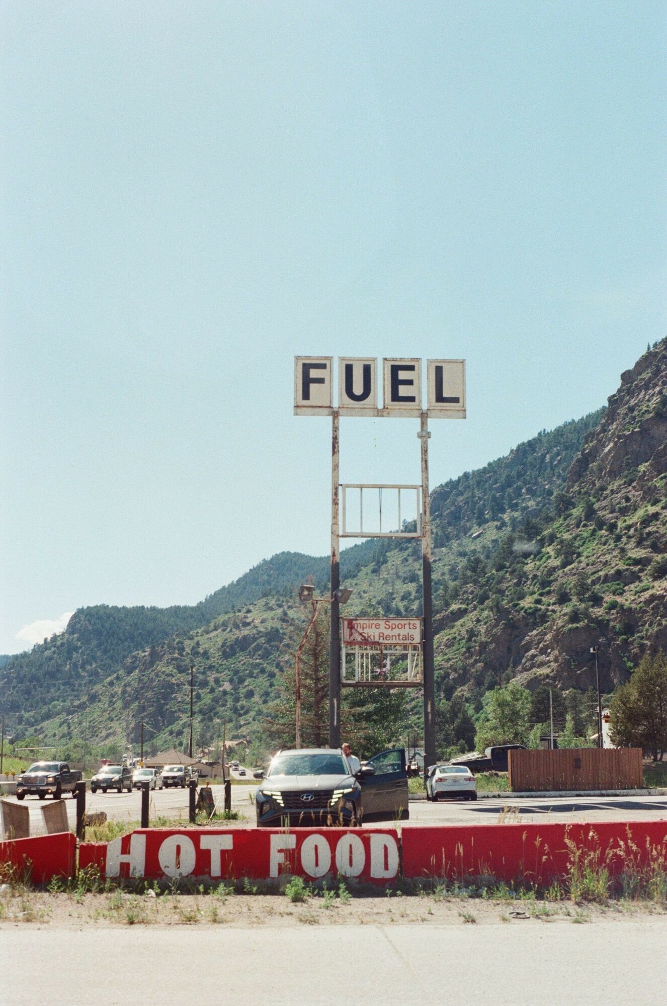 Fuel sign with a mountain background, parking lot, and a red and white sign reading 