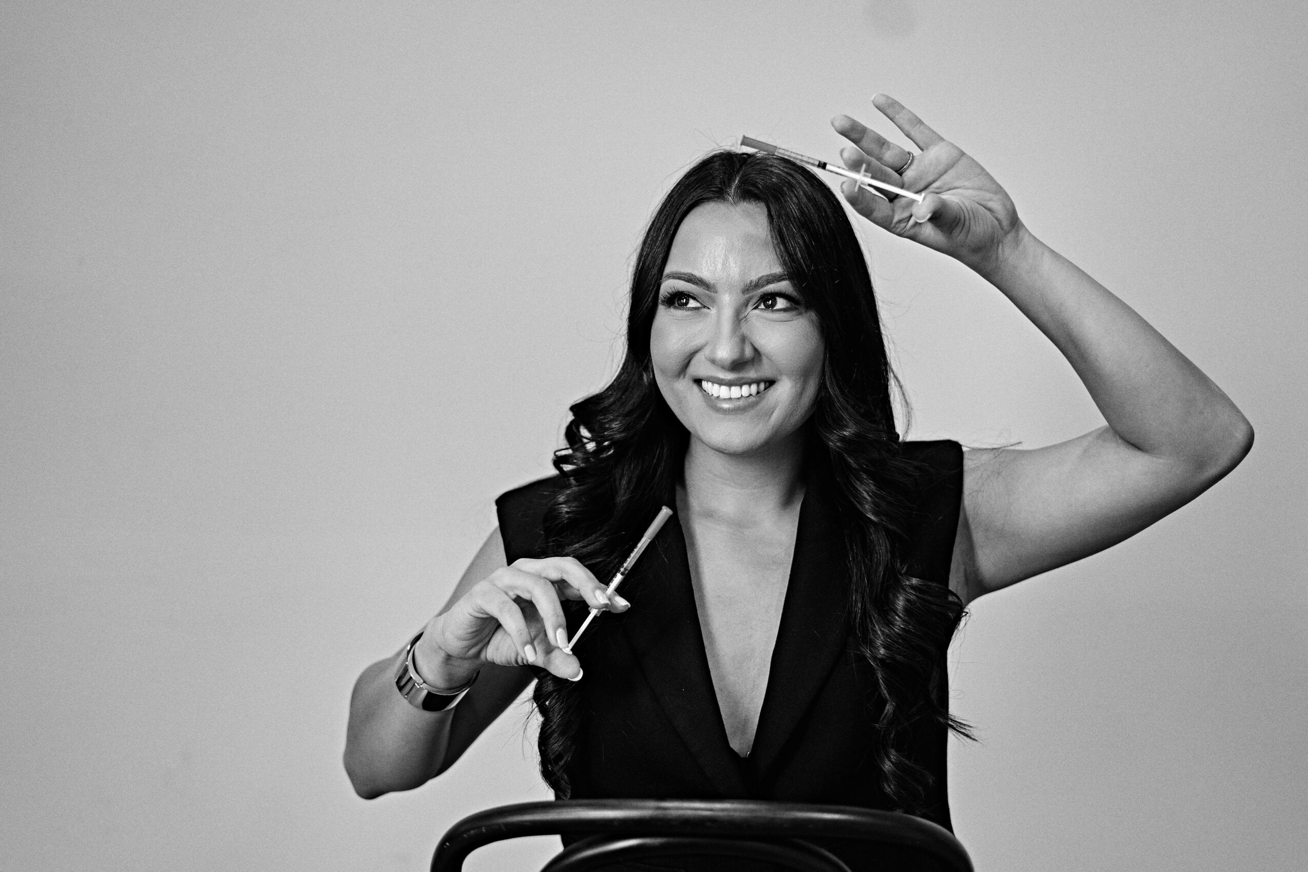 Woman smiling, holding a pen, with her right hand raised in a wave, in black and white.