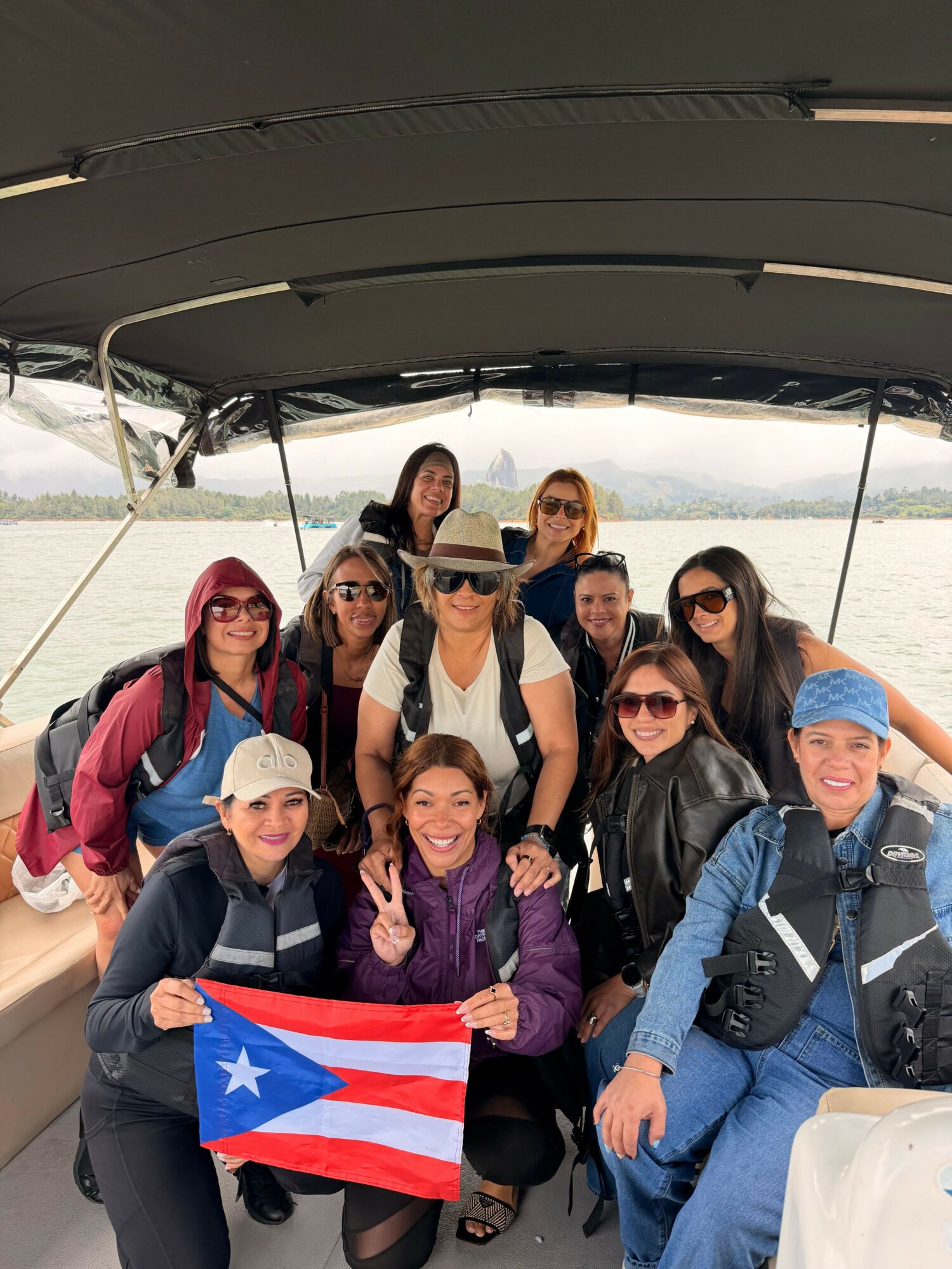 Group of ten people on a boat, some holding a Puerto Rican flag, with water and mountains in background.