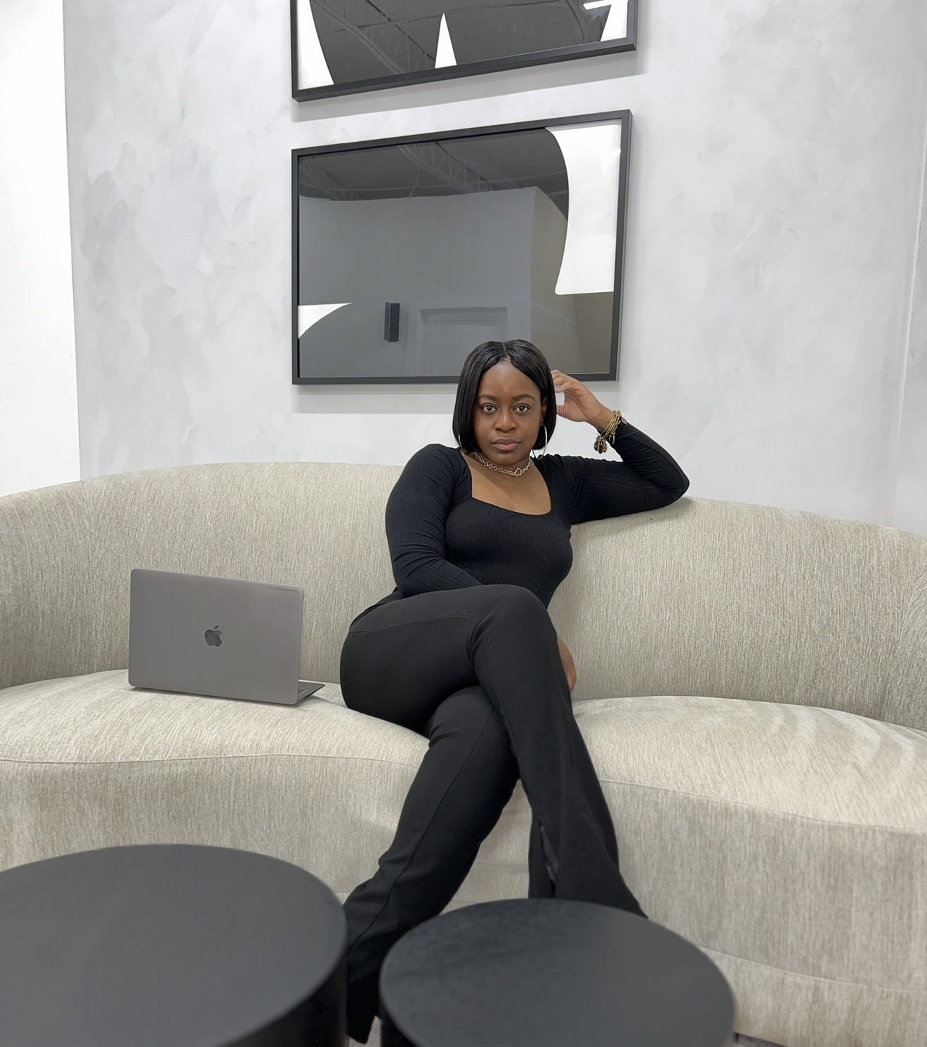 Woman sitting on a beige sofa with a laptop beside her, in a modern room with abstract wall art.