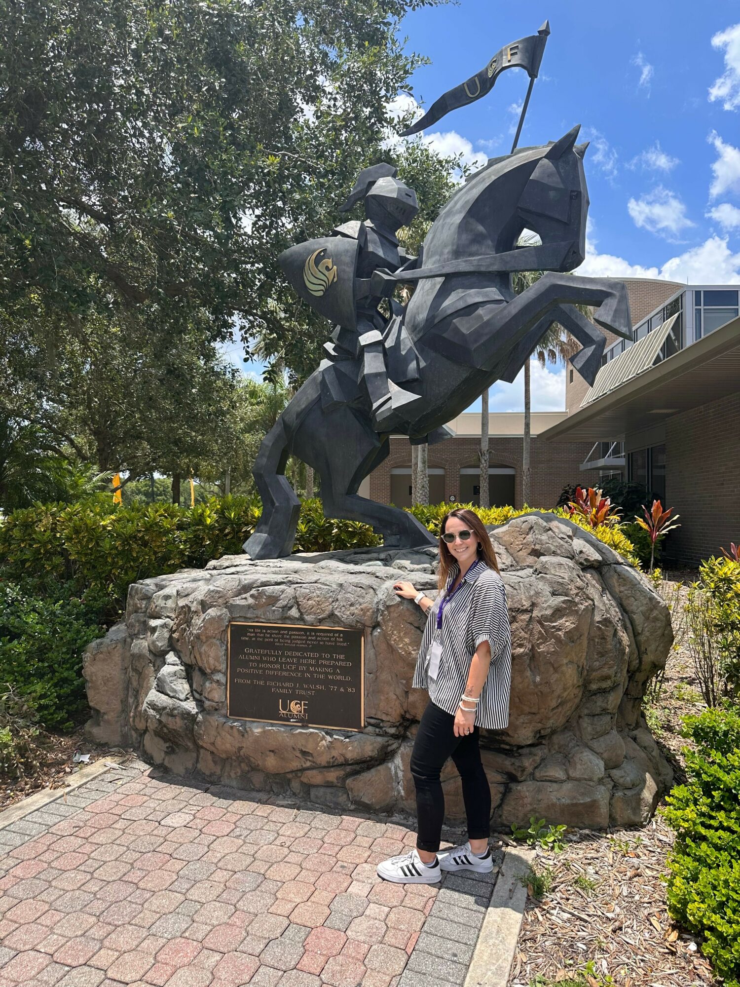 Woman standing in front of a large mounted statue of a knight on a horse, with a plaque on the rock base.