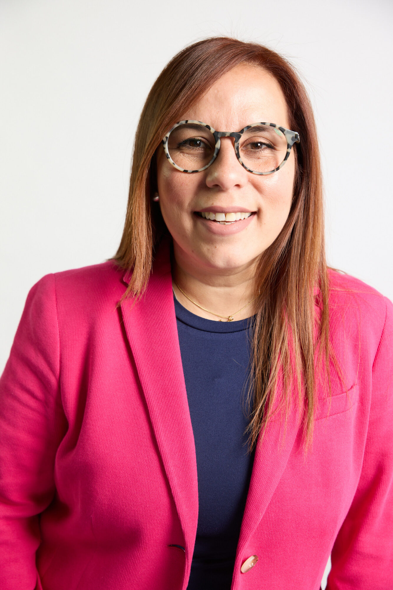 Woman with long hair, glasses, wearing a pink blazer and dark shirt, smiling at camera.