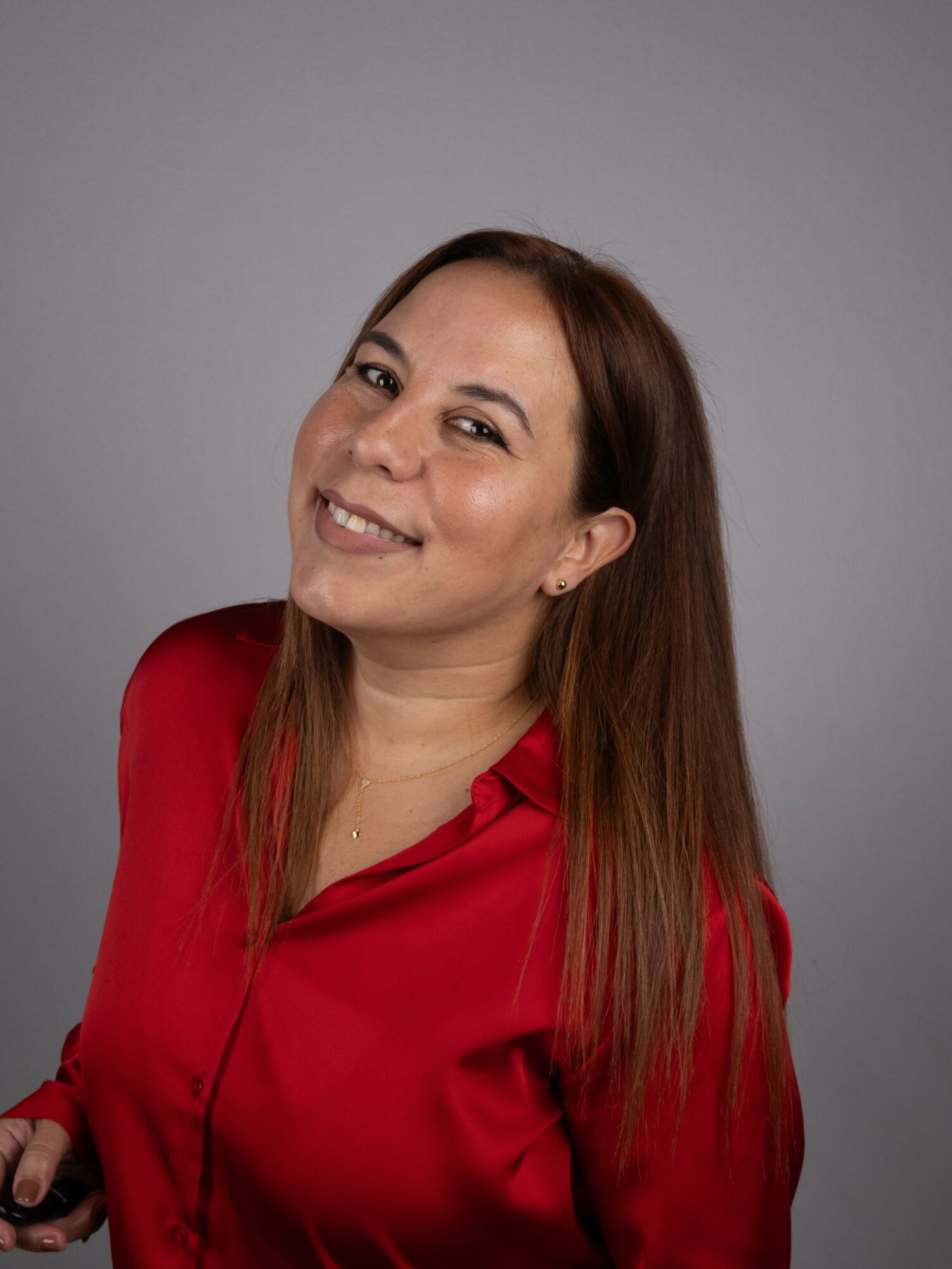Smiling woman with long brown hair wearing a red blouse against a gray background.