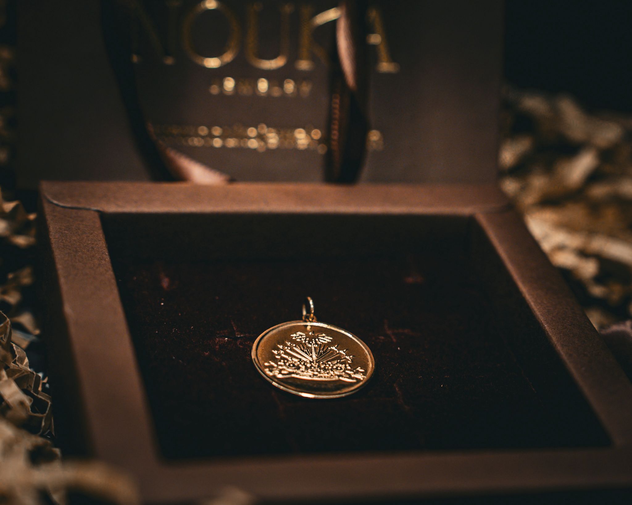 Gold pendant with engraved design inside a black box with a textured surface.