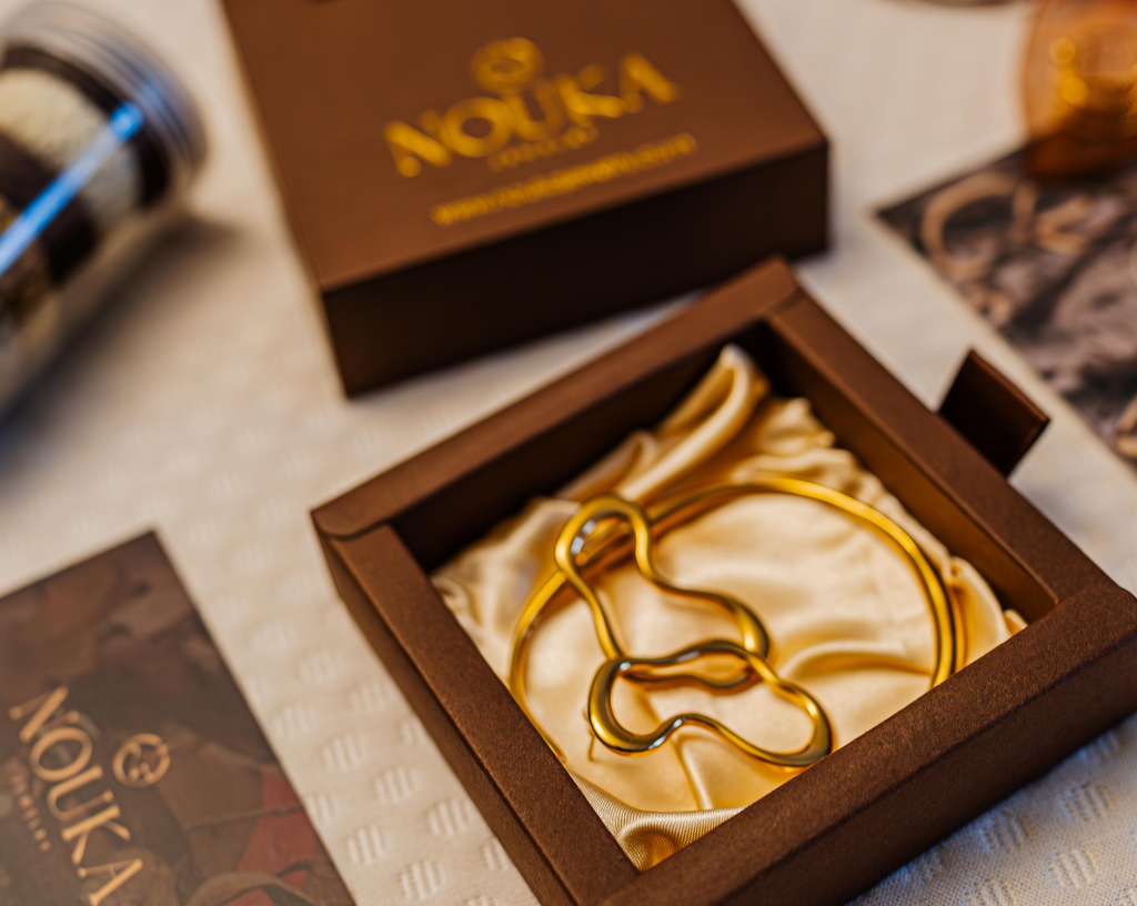 Gold necklace inside a brown box with a cream-colored interior, surrounded by photographs and a brown box.
