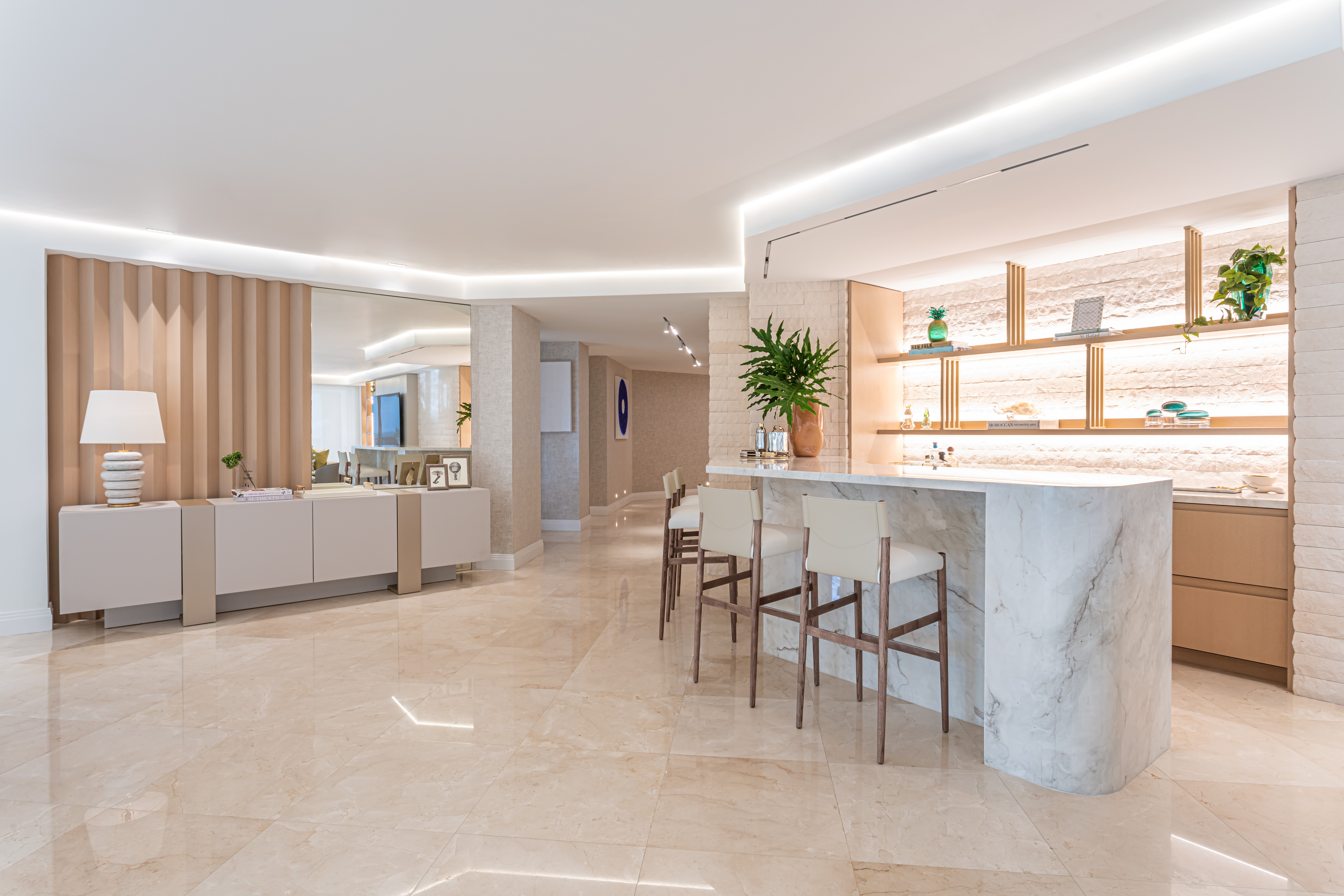 Open living space with a marble kitchen island, bar stools, a sofa, and decorative plants, illuminated by natural light.