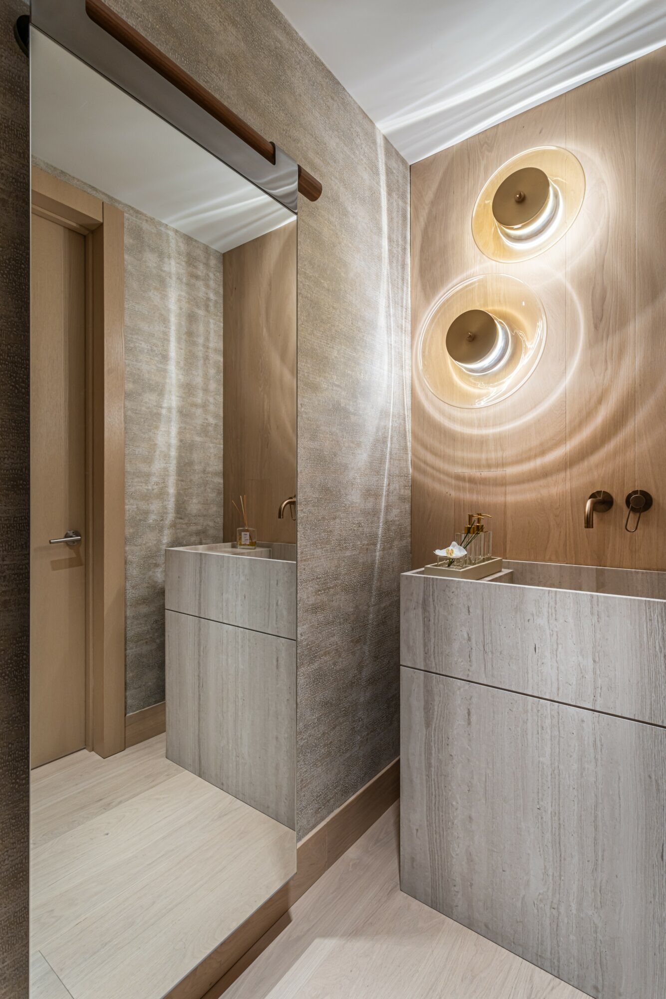 Bathroom with textured beige wall, two circular wall lights, gray vanity, and wooden door.