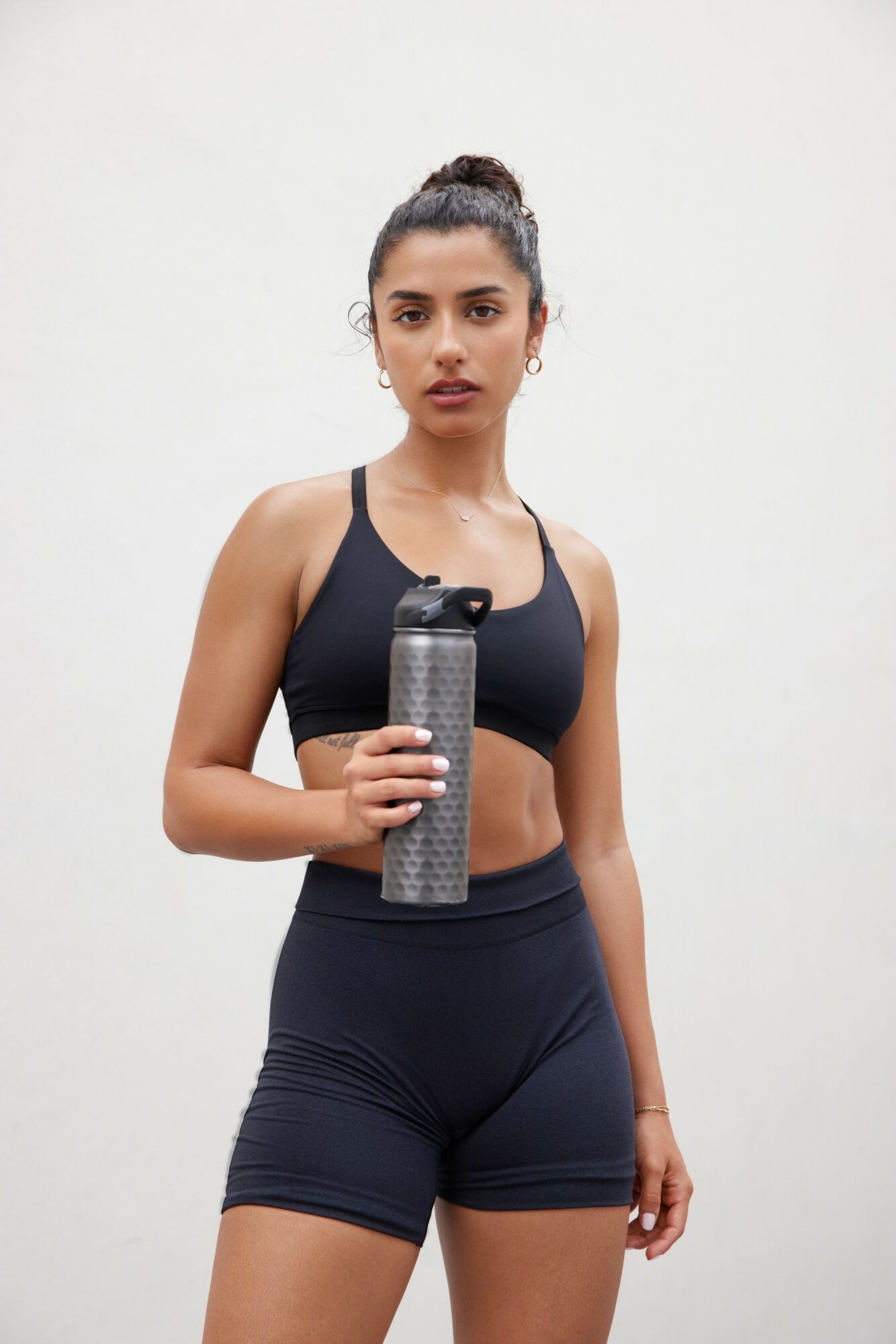 Woman in athletic wear holding a water bottle, standing against a plain background.