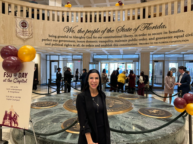 Woman standing in front of a fountain with a banner about Florida history and people, surrounded by a rope barrier.