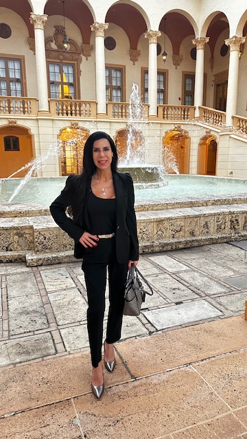 Woman in black outfit standing in front of a fountain with arches and columns in a courtyard.