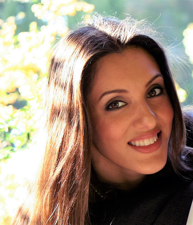 Close-up of smiling woman with long hair outdoors, sunlight on hair, blurred green background.