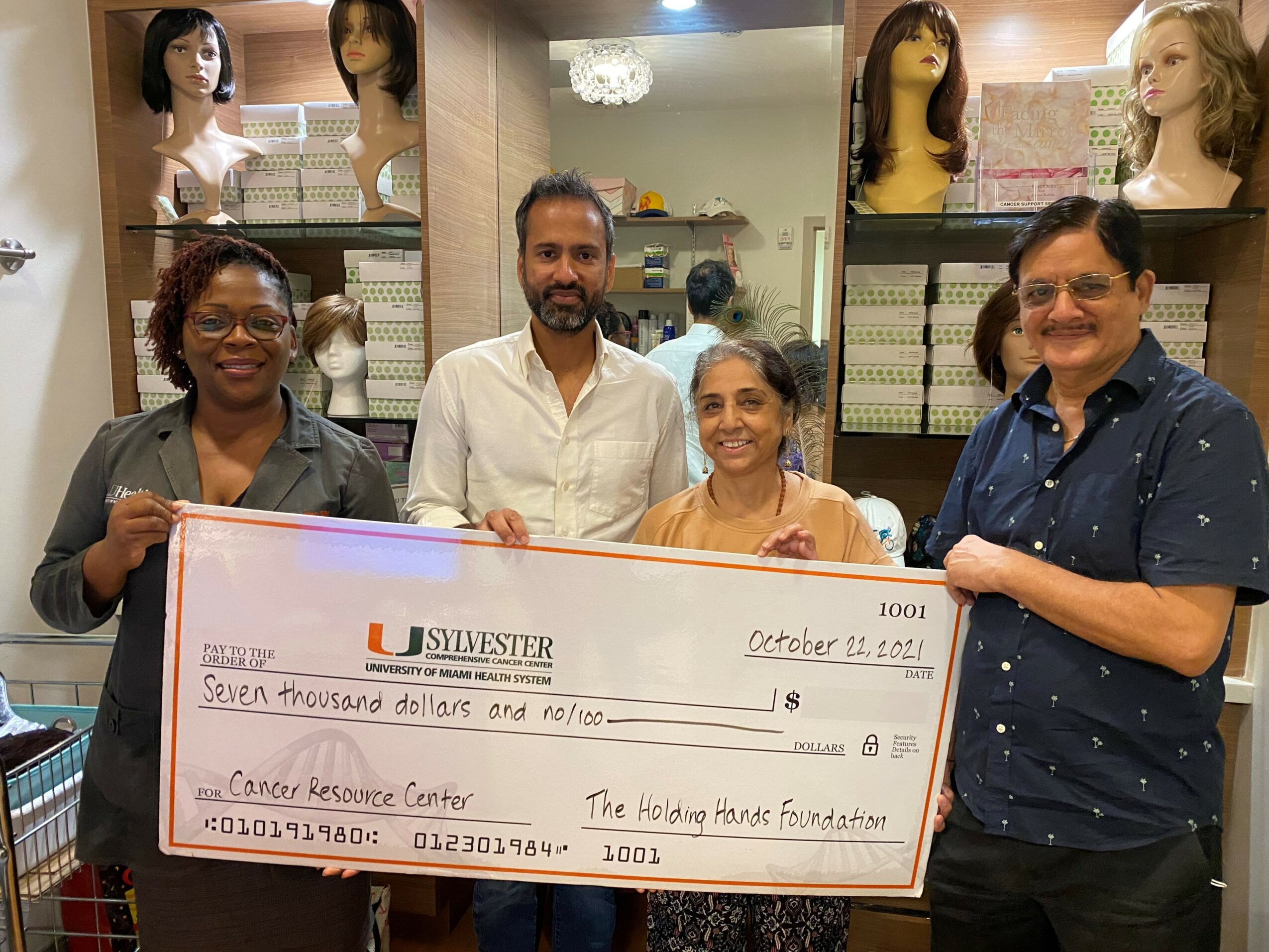 Four people holding a large check in a store with mannequin heads and hair products in the background.