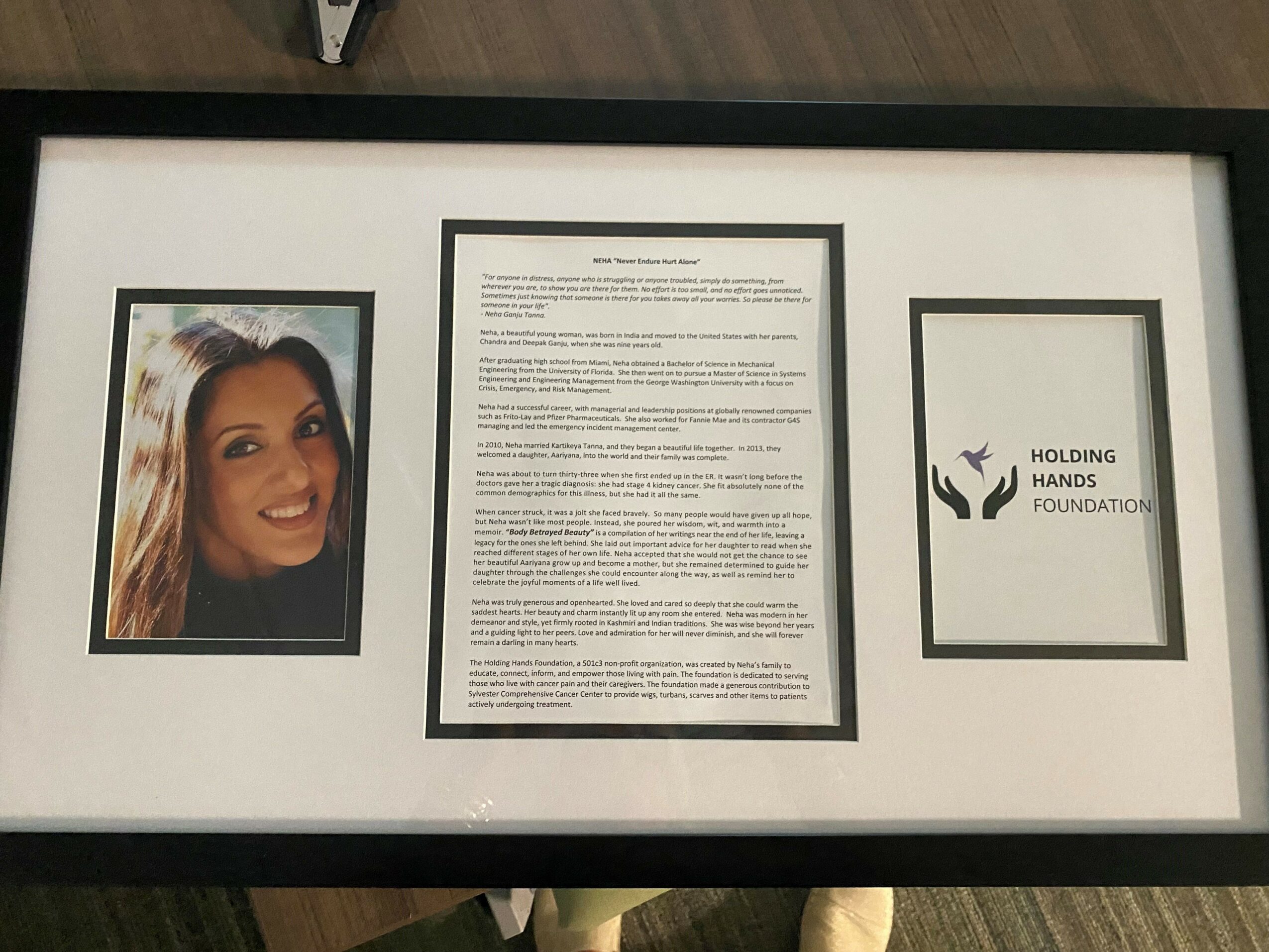 Framed display with a portrait of a smiling woman on the left, a document in the center, and a logo on the right.