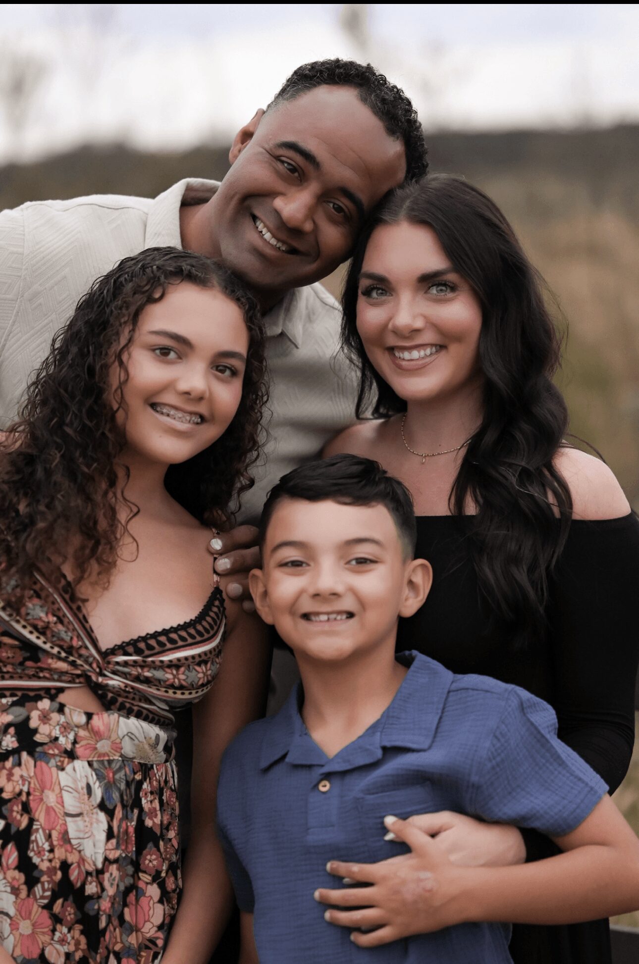 Four people smiling outdoors, two adults and two children, standing close together.