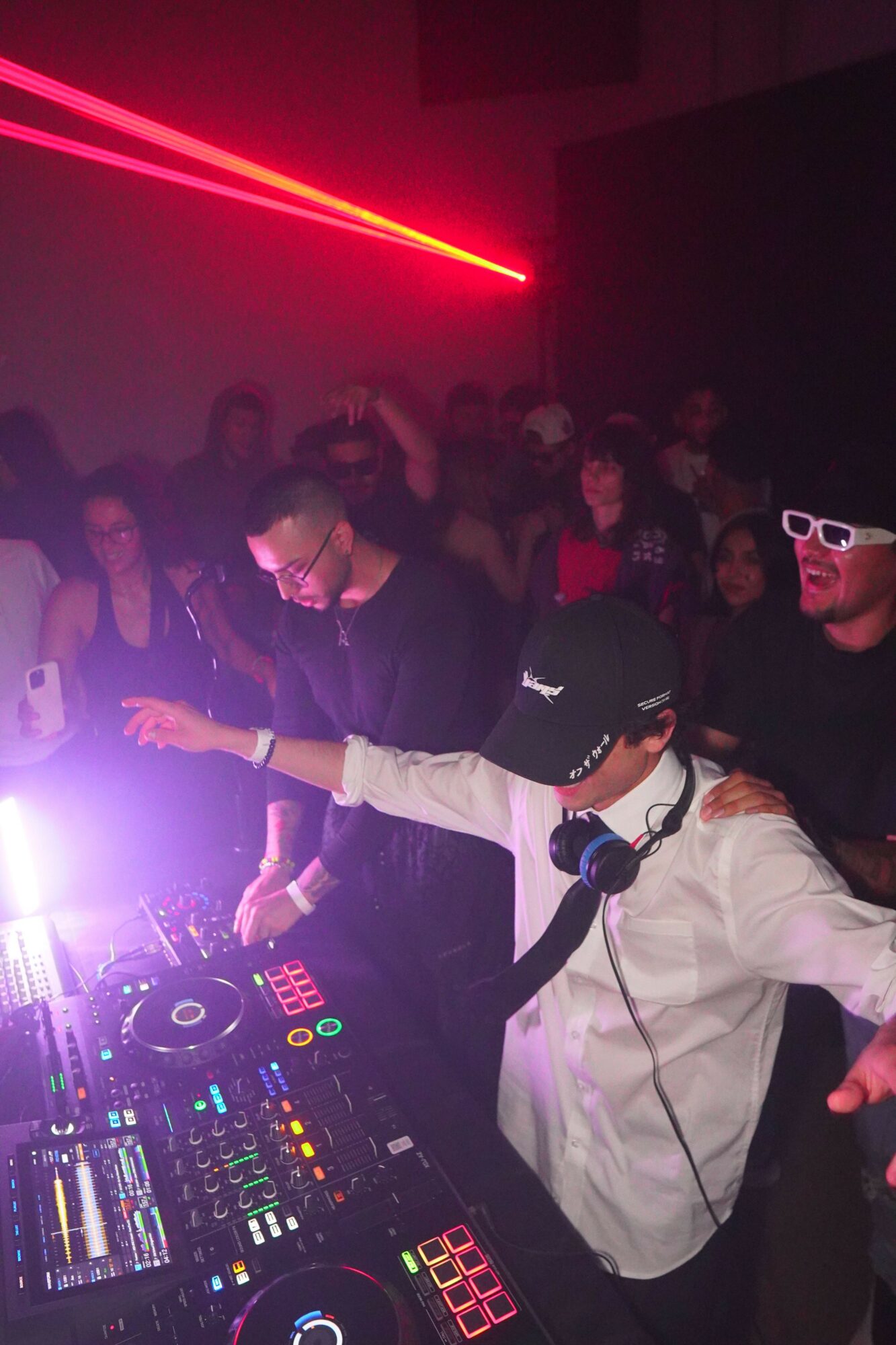 DJ wearing headphones and sunglasses, mixing music at a crowded nightclub with colorful lighting.