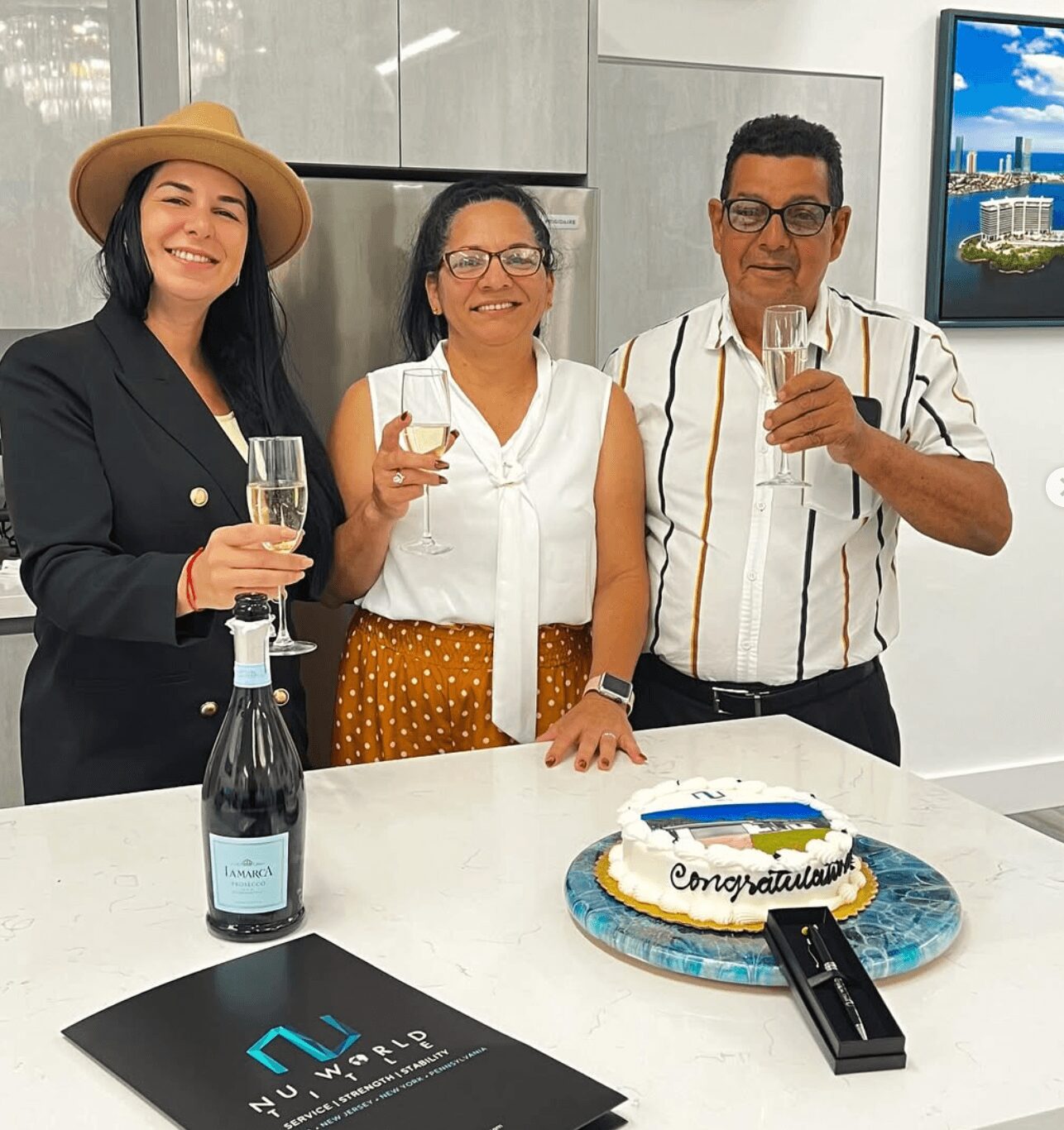 Three people celebrating with a cake and champagne in a modern room, smiling at the camera.