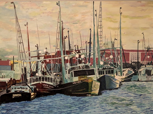 Several sailboats docked at a harbor with buildings in the background, water in the foreground, and a cloudy sky.