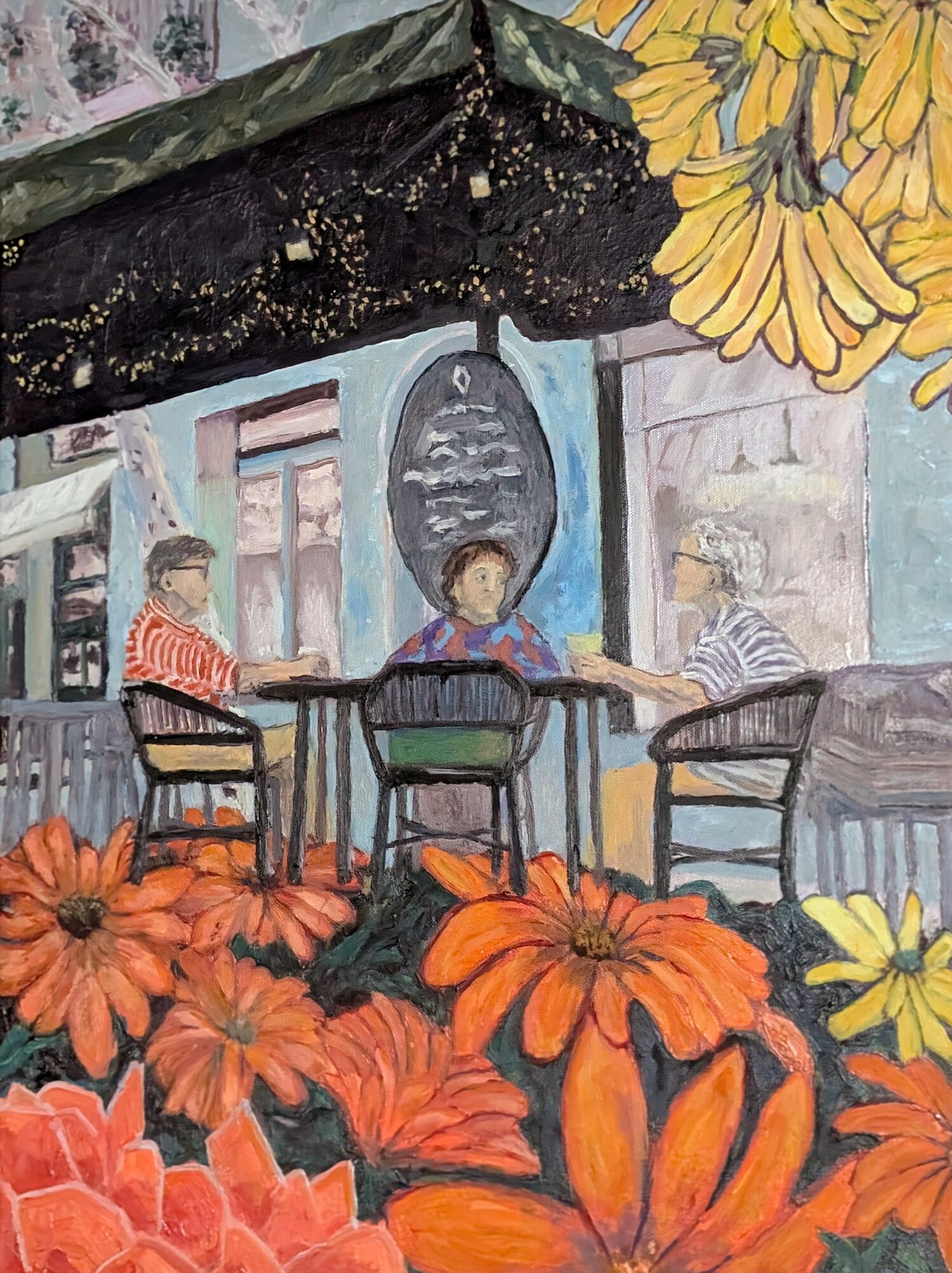 Three people sit at a table outdoors with orange flowers in foreground and a mural background.
