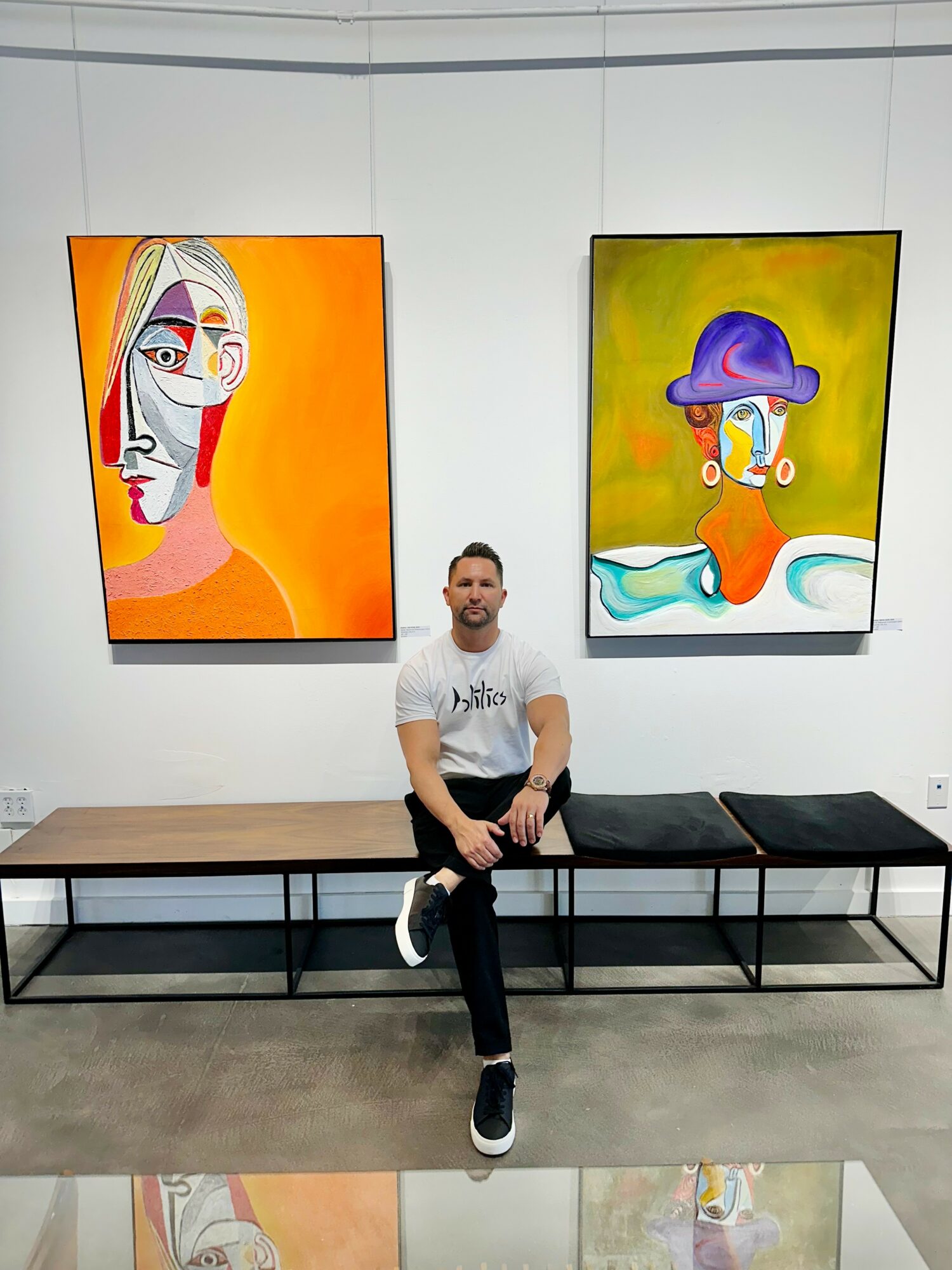 Man sitting on a bench in an art gallery with two colorful abstract paintings behind him.