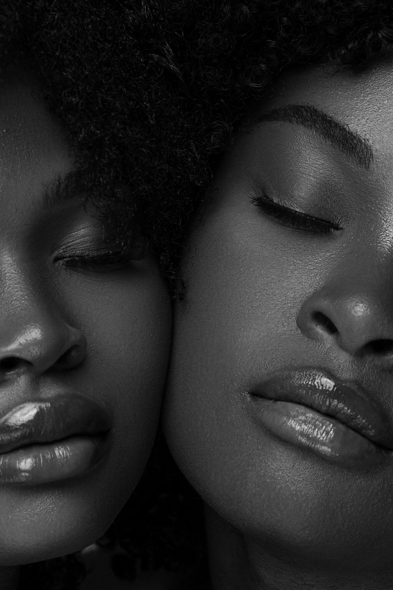 Close-up of two women with closed eyes and glossy lips, sharing an intimate moment.