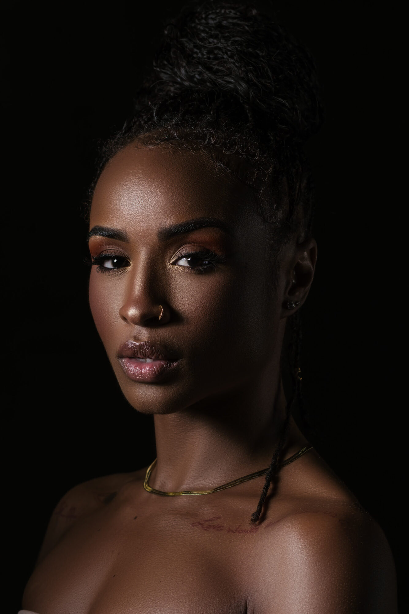 Portrait of a woman with dark hair styled in a bun, looking directly at the camera against a black background.