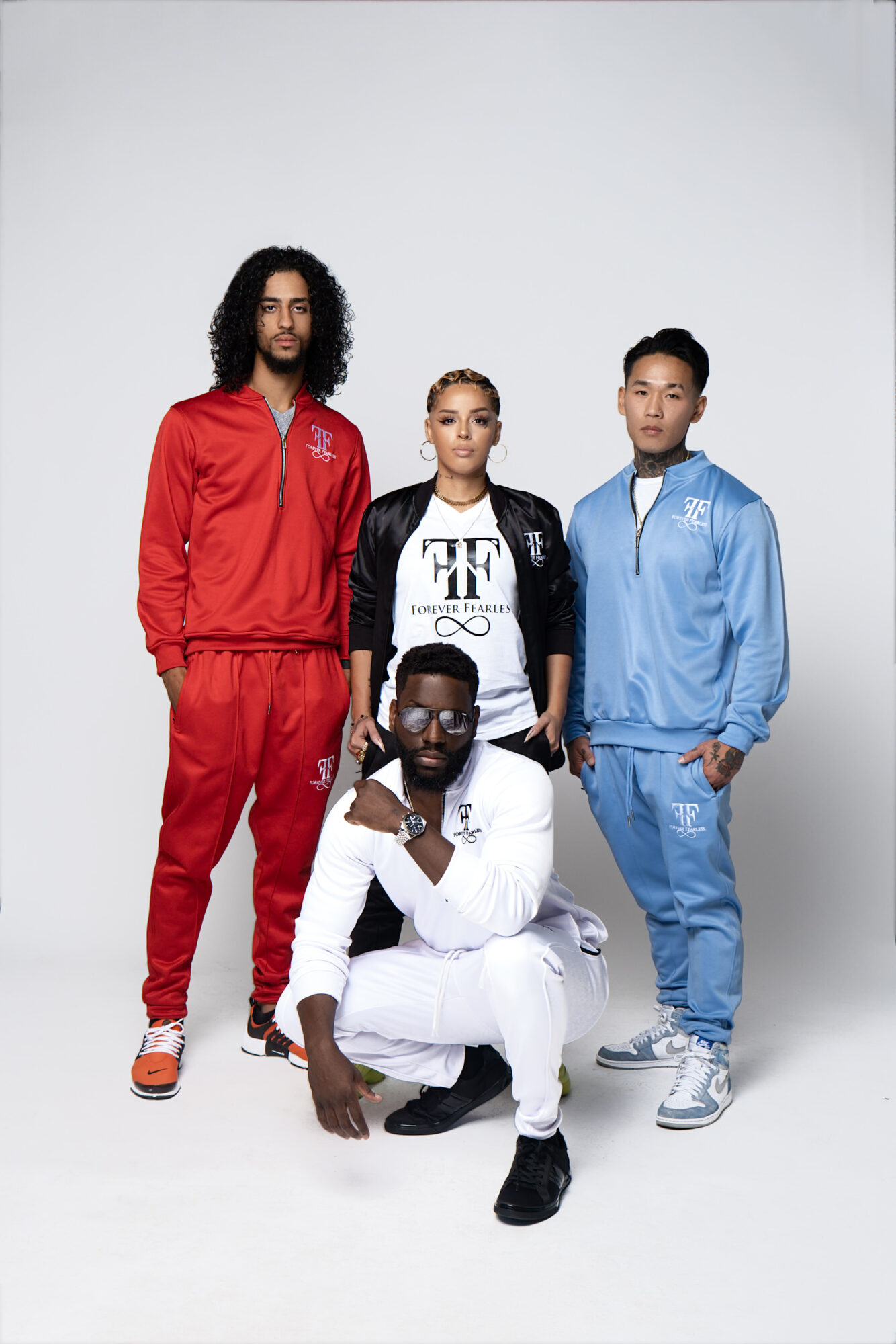 Four athletes pose together, two standing and two kneeling, wearing sportswear in red, black, blue, and white, against a plain background.