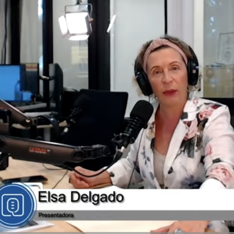 Woman with short hair wearing headphones speaking into a microphone in a radio studio.