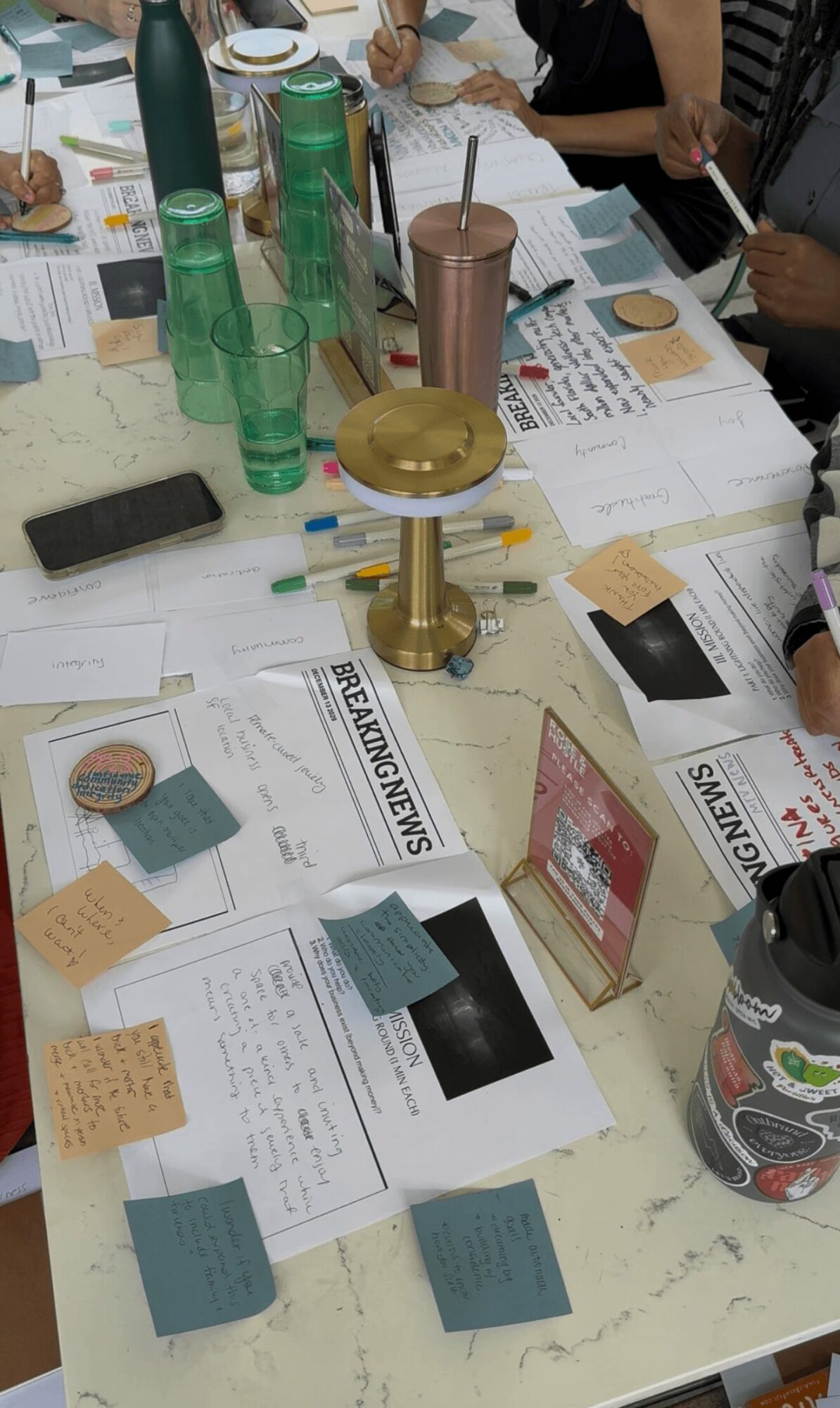 Table with papers, sticky notes, a candle holder, drinks, and a person holding a tablet.