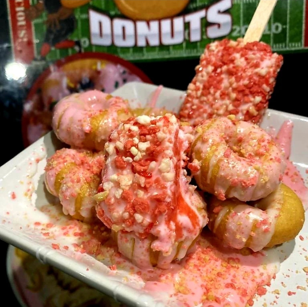 Plate of pink and yellow dipped ice cream bars with sprinkles and toppings on a white dish.