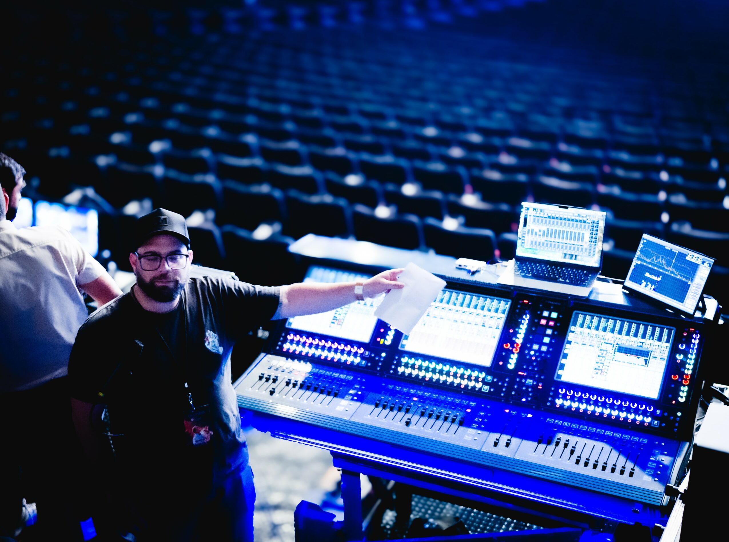 Person operating sound mixing equipment with empty auditorium in background.