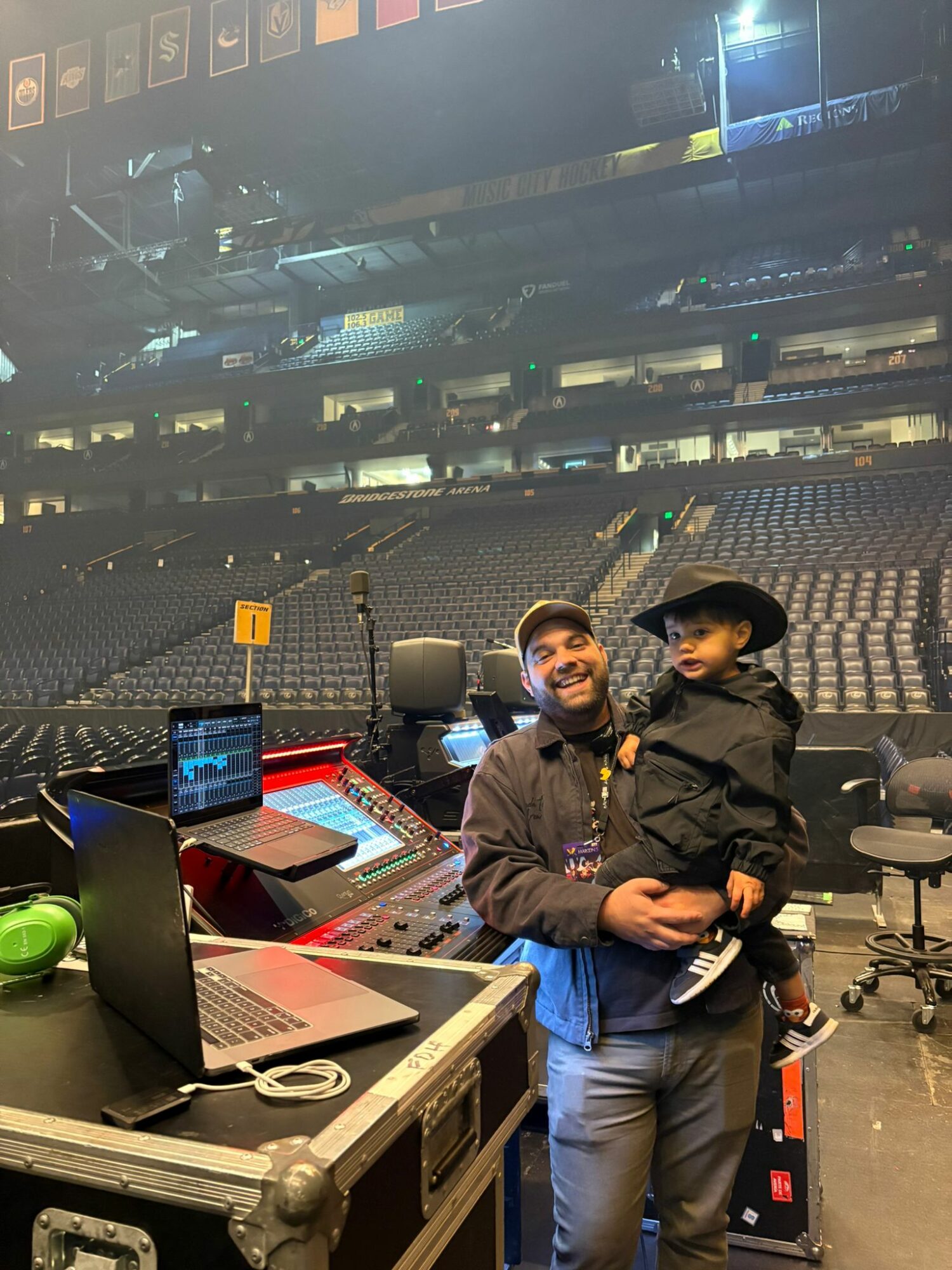 Man holding a child on stage with audio equipment and empty seats in the background.