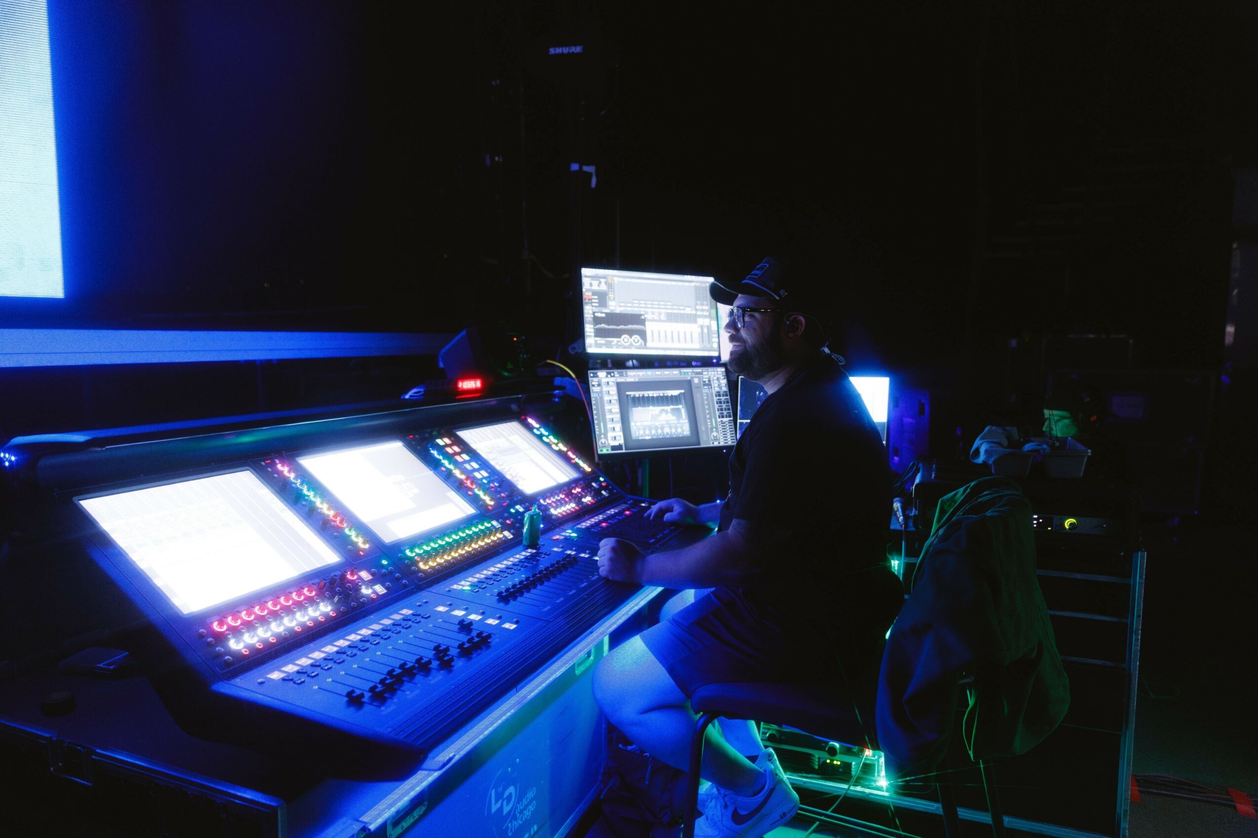 Person working at a large illuminated control panel with multiple screens in a dark environment.