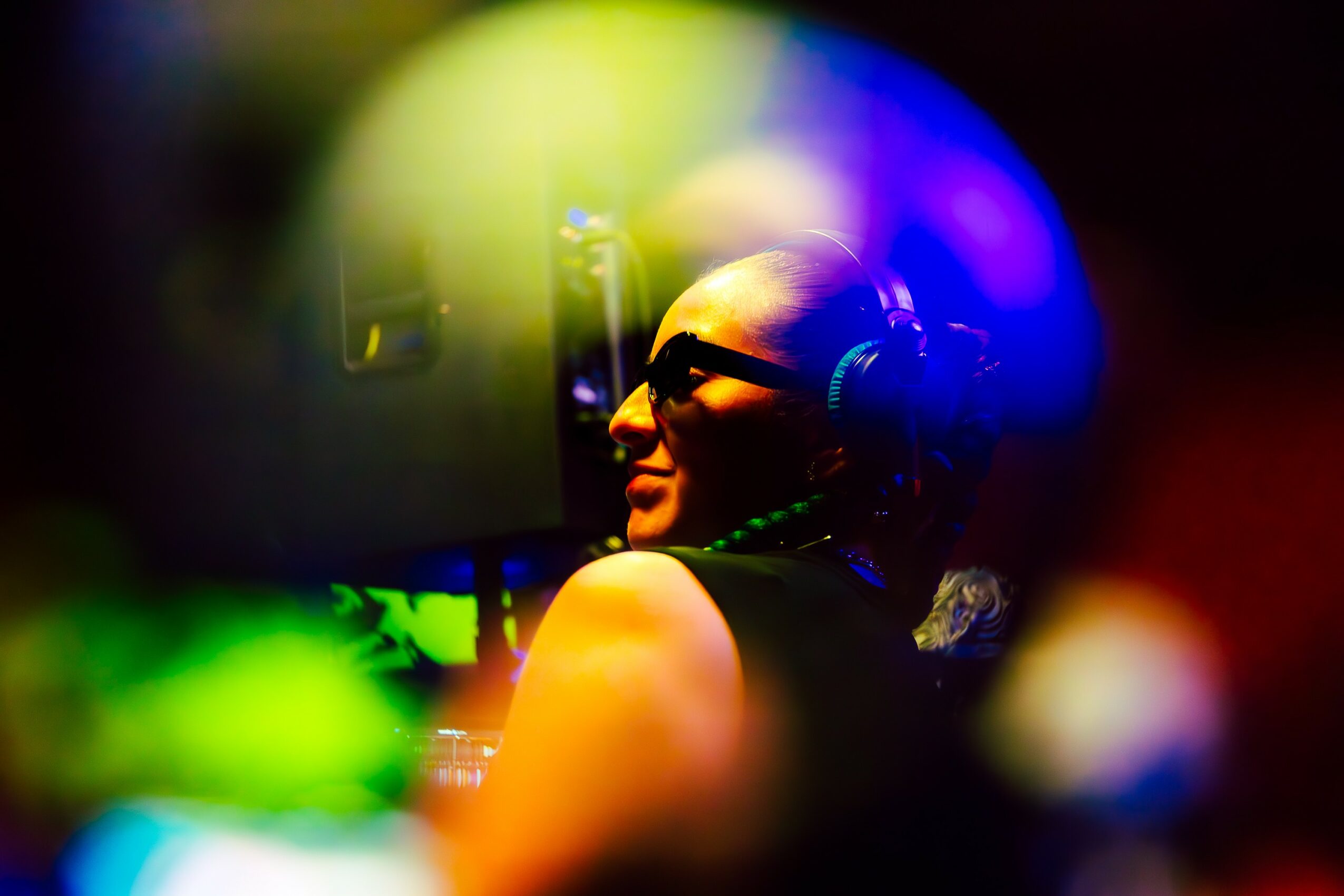 Person wearing headphones and glasses, looking at a screen with colorful reflections around.