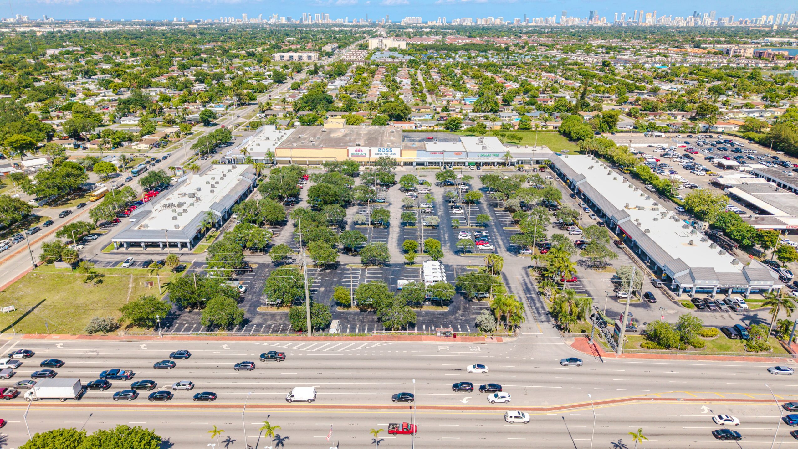 Aerial view of a commercial area with parking lots, buildings, and a highway in the foreground.