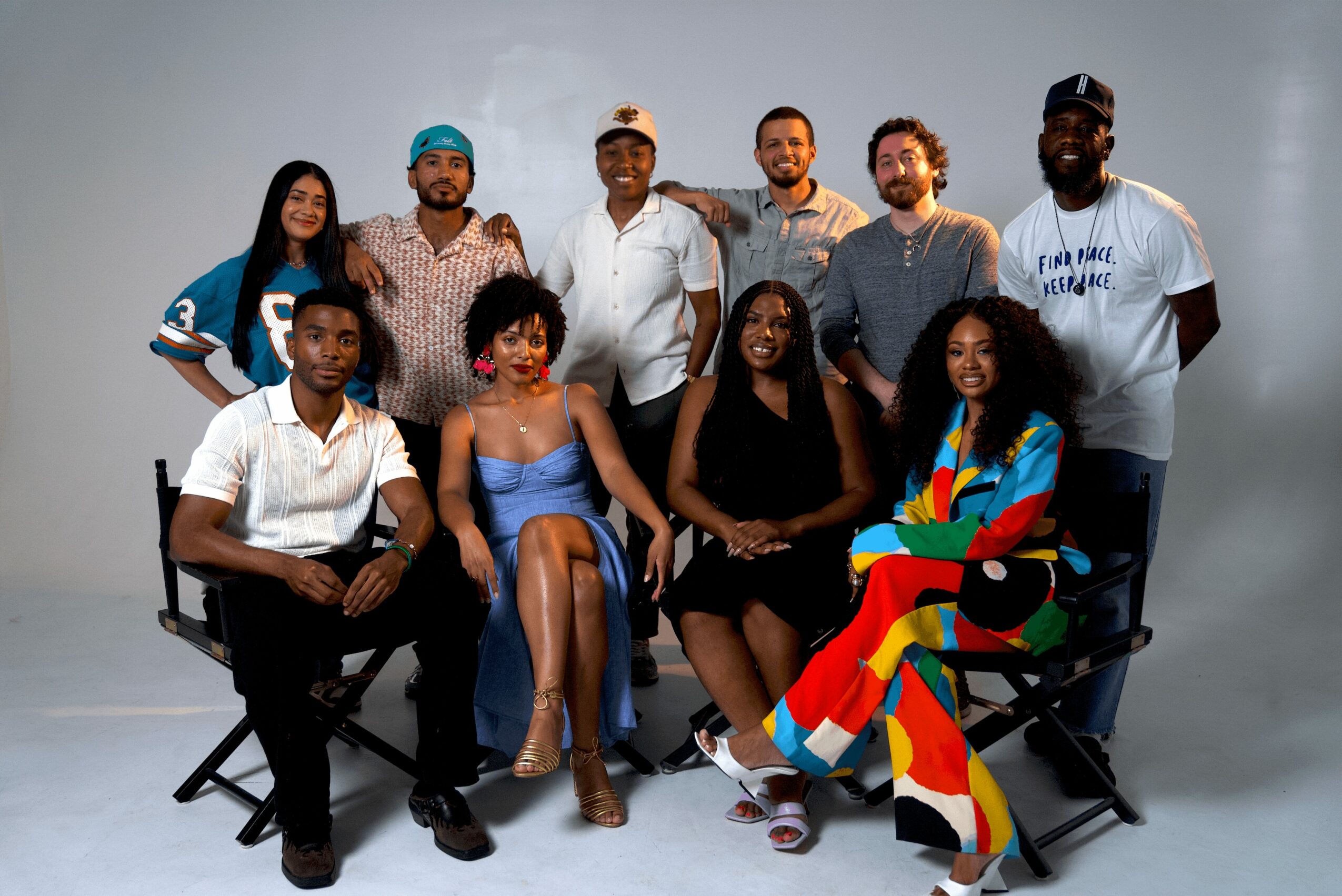 Group of ten diverse people posing together, some sitting and some standing, in a studio setting.