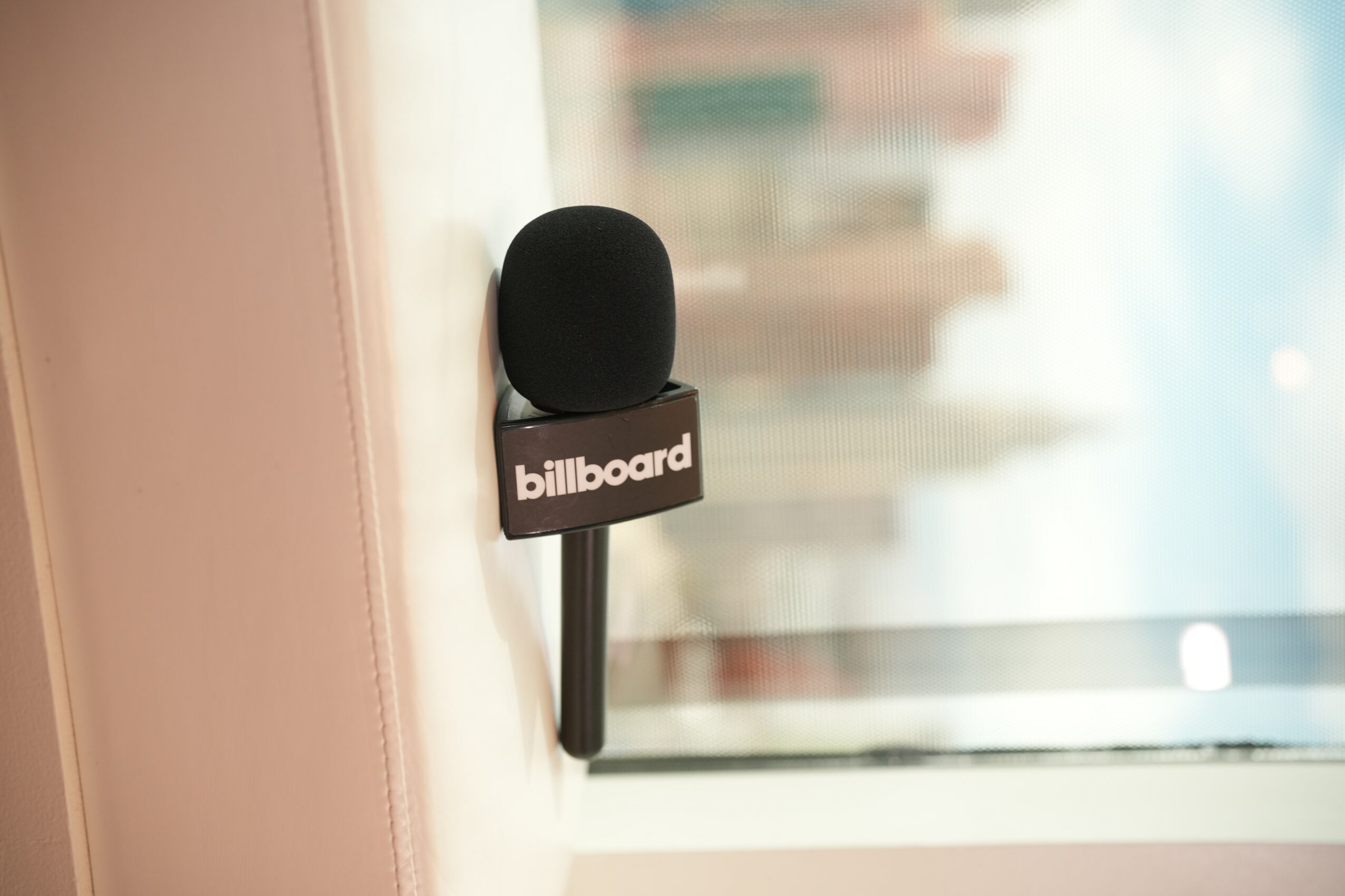 Black microphone with a black base labeled 'billboard' in front of a window with a blurred cityscape background.