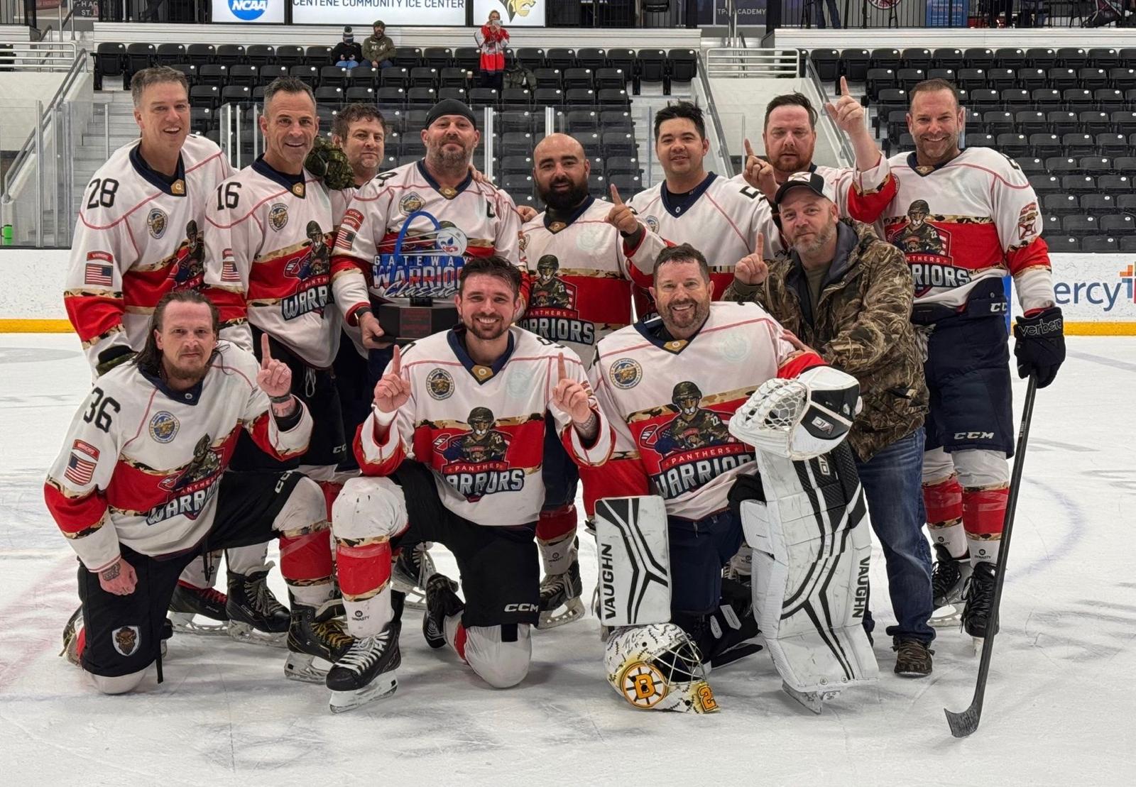 Group of ice hockey players in team uniforms on ice rink, some kneeling, some standing, holding hockey sticks.