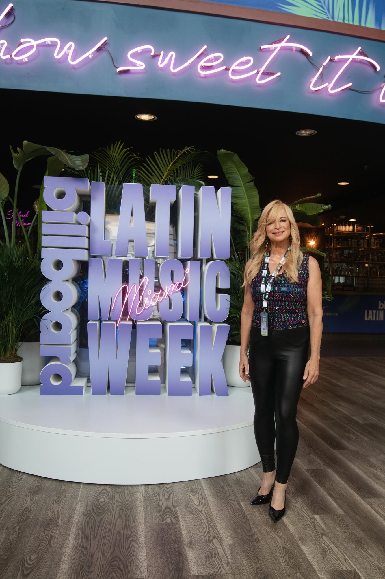 Woman standing next to a sign that reads 'Latin Music Week' with neon lights above.