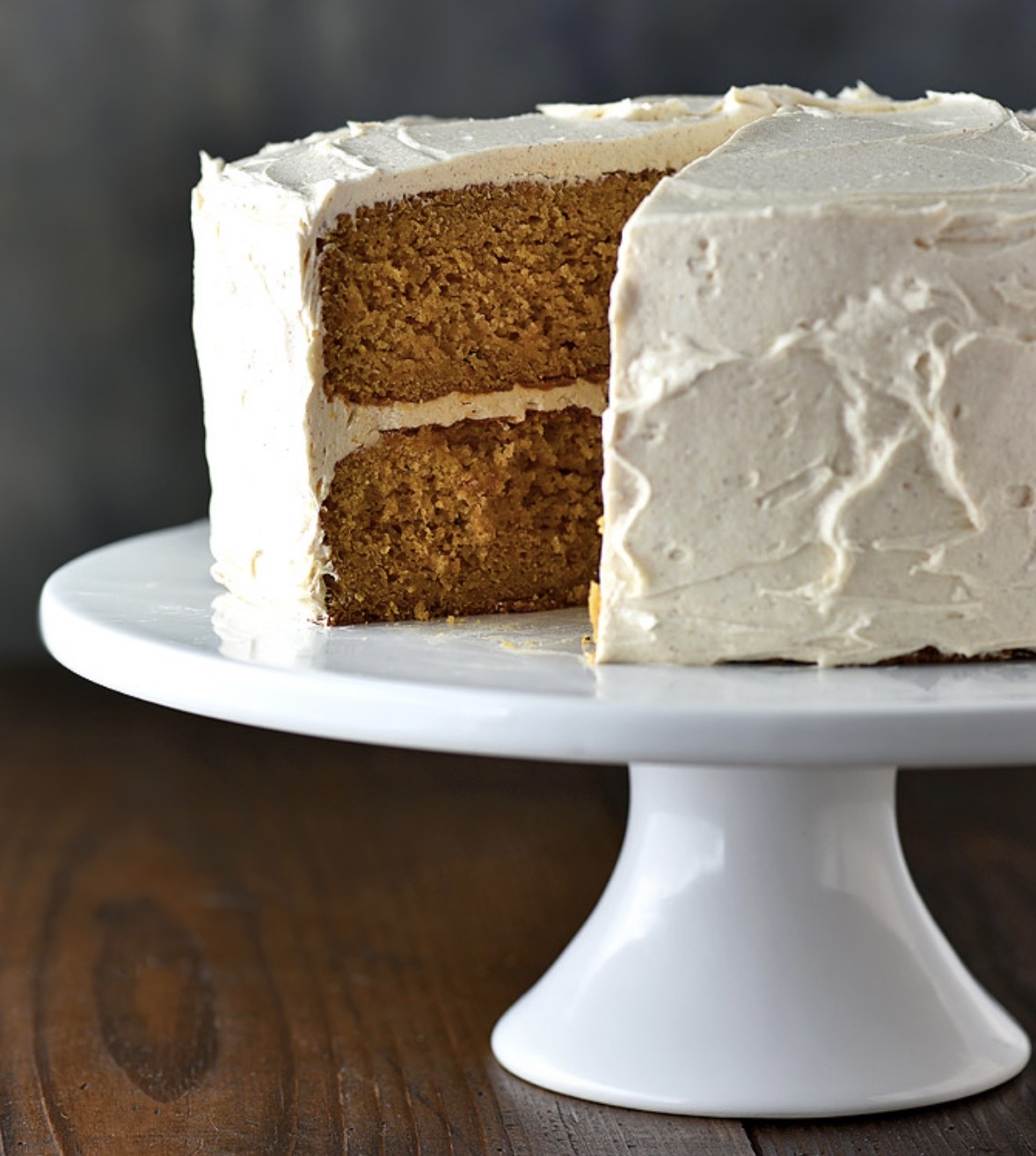 Slice of layered cake with white frosting on a white cake stand, showing two layers of cake inside.