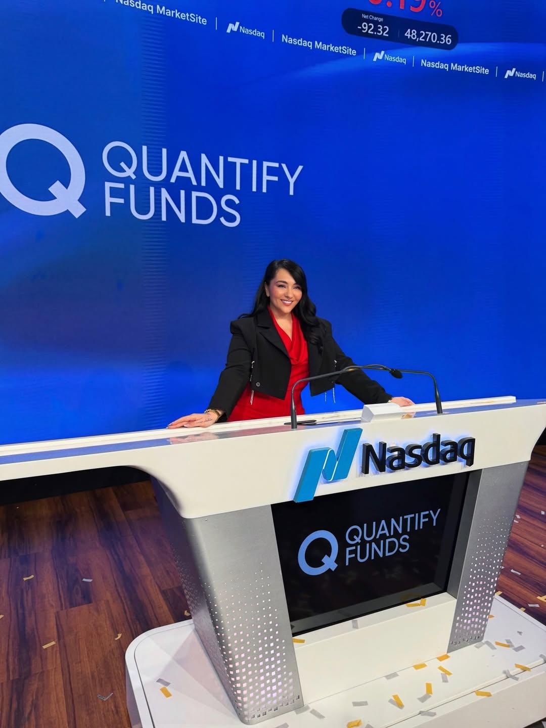 Woman standing at a podium with Nasdaq and Quantify Funds logos, smiling, in a conference room.