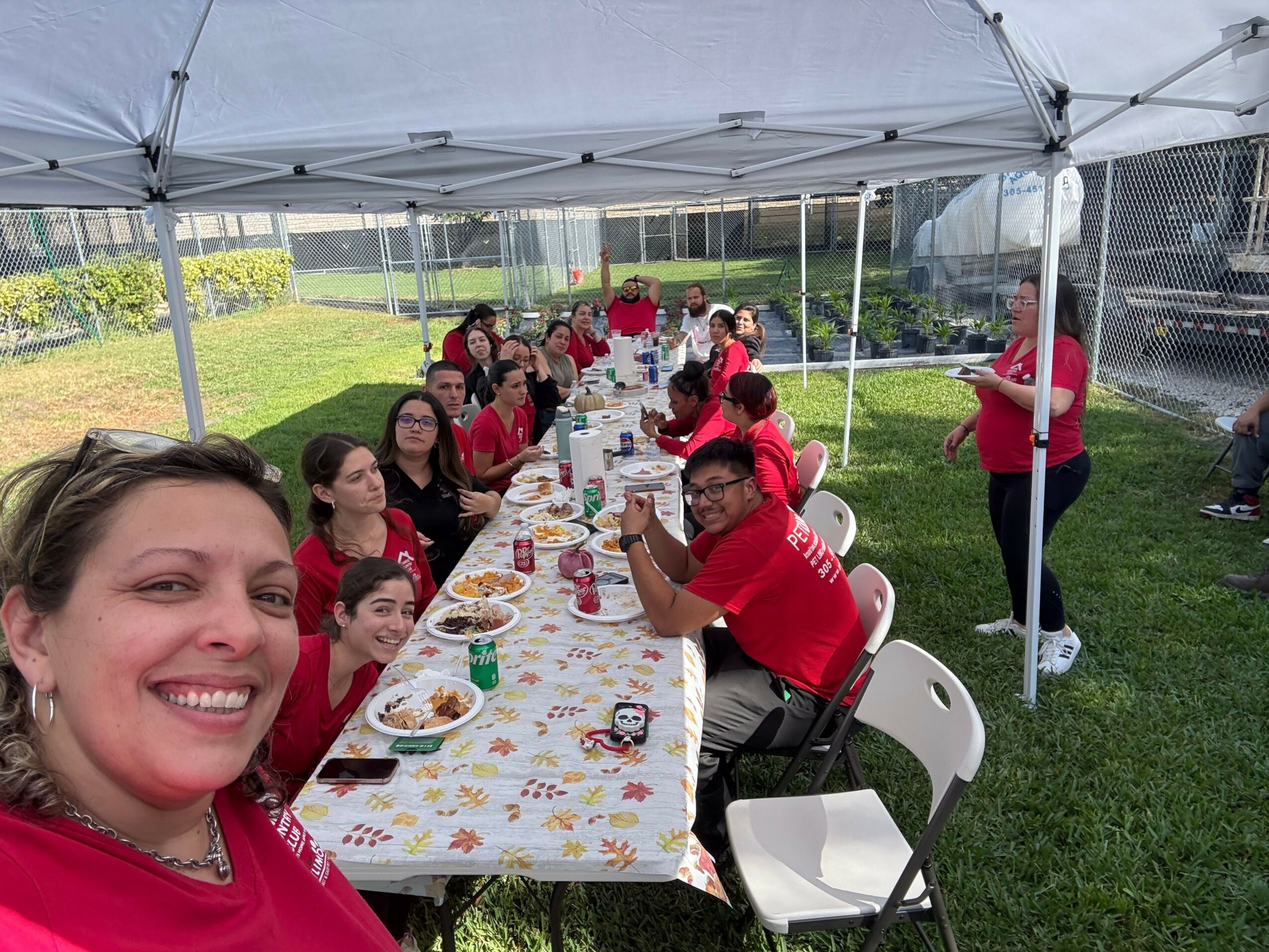 Group of people sitting at a long table outdoors under a canopy, enjoying a meal together.