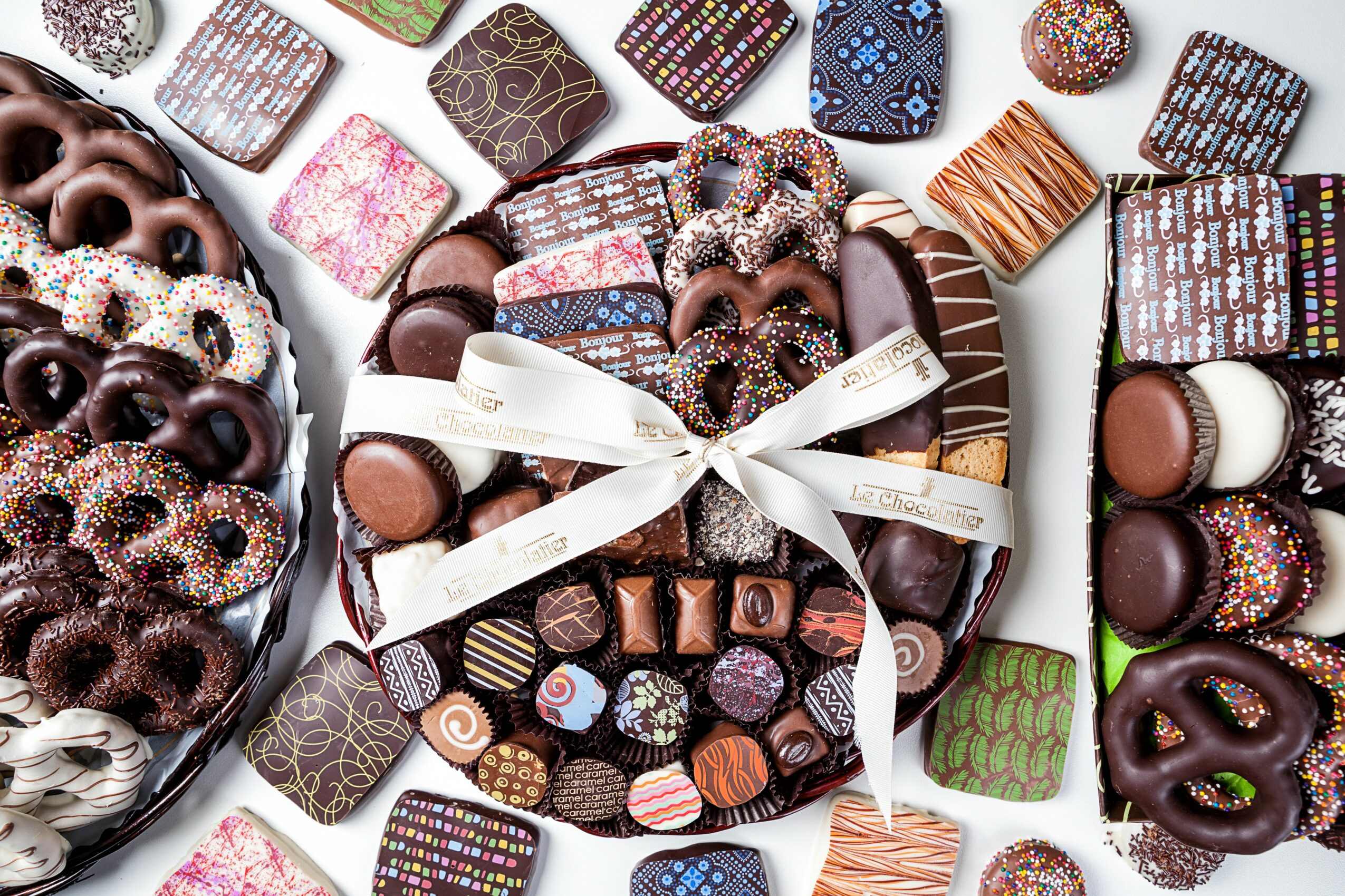 Assorted chocolates and donuts arranged on white plates with a ribbon in the center.