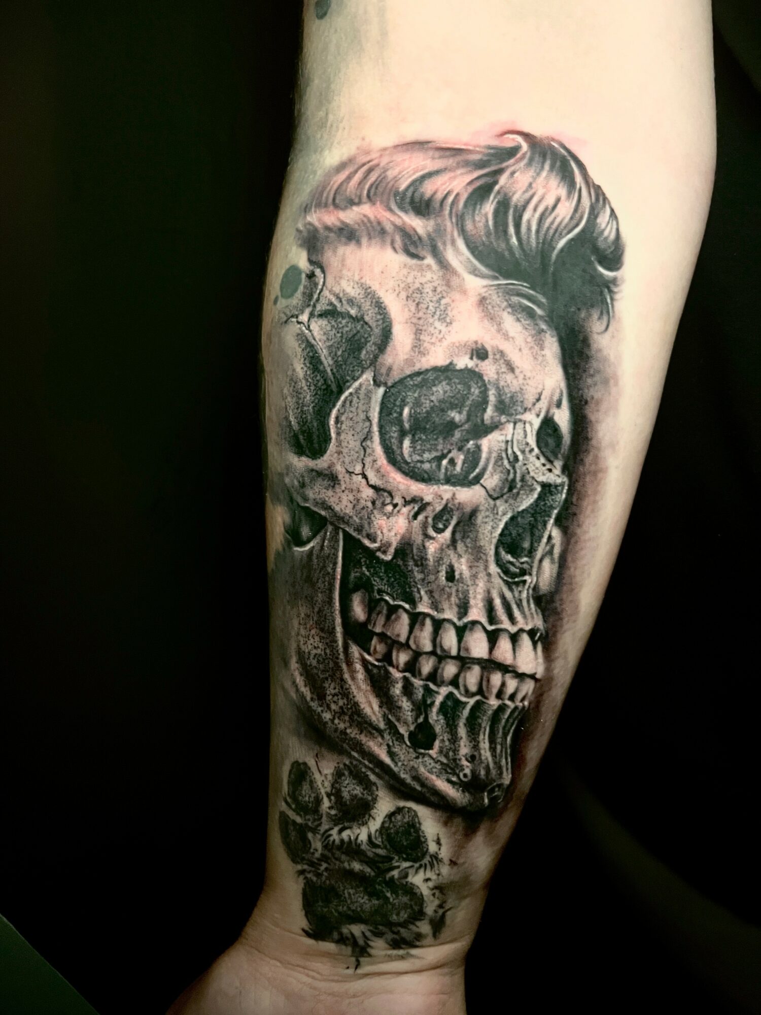 Tattoo of a skull with a hairstyle, detailed with shading and a dark background.