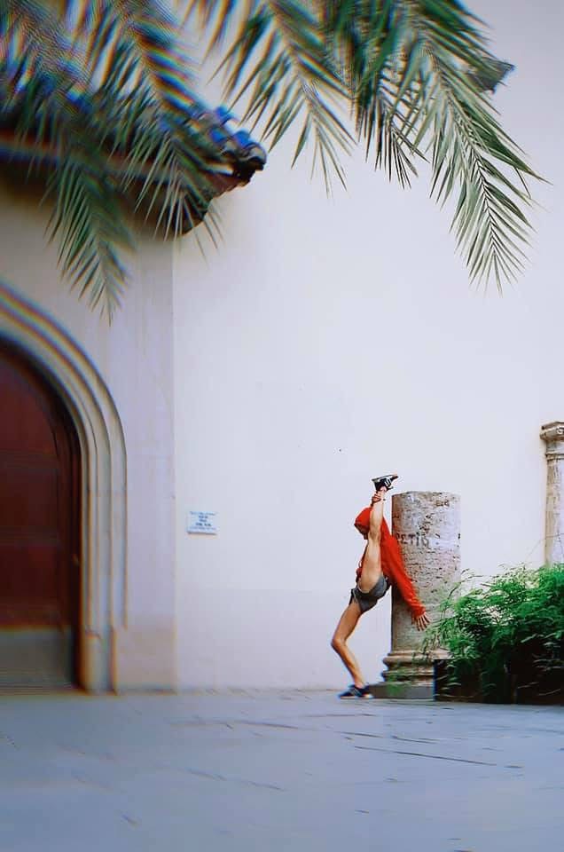 Person standing near a column with palm tree branches overhead, wearing a red jacket and shorts.