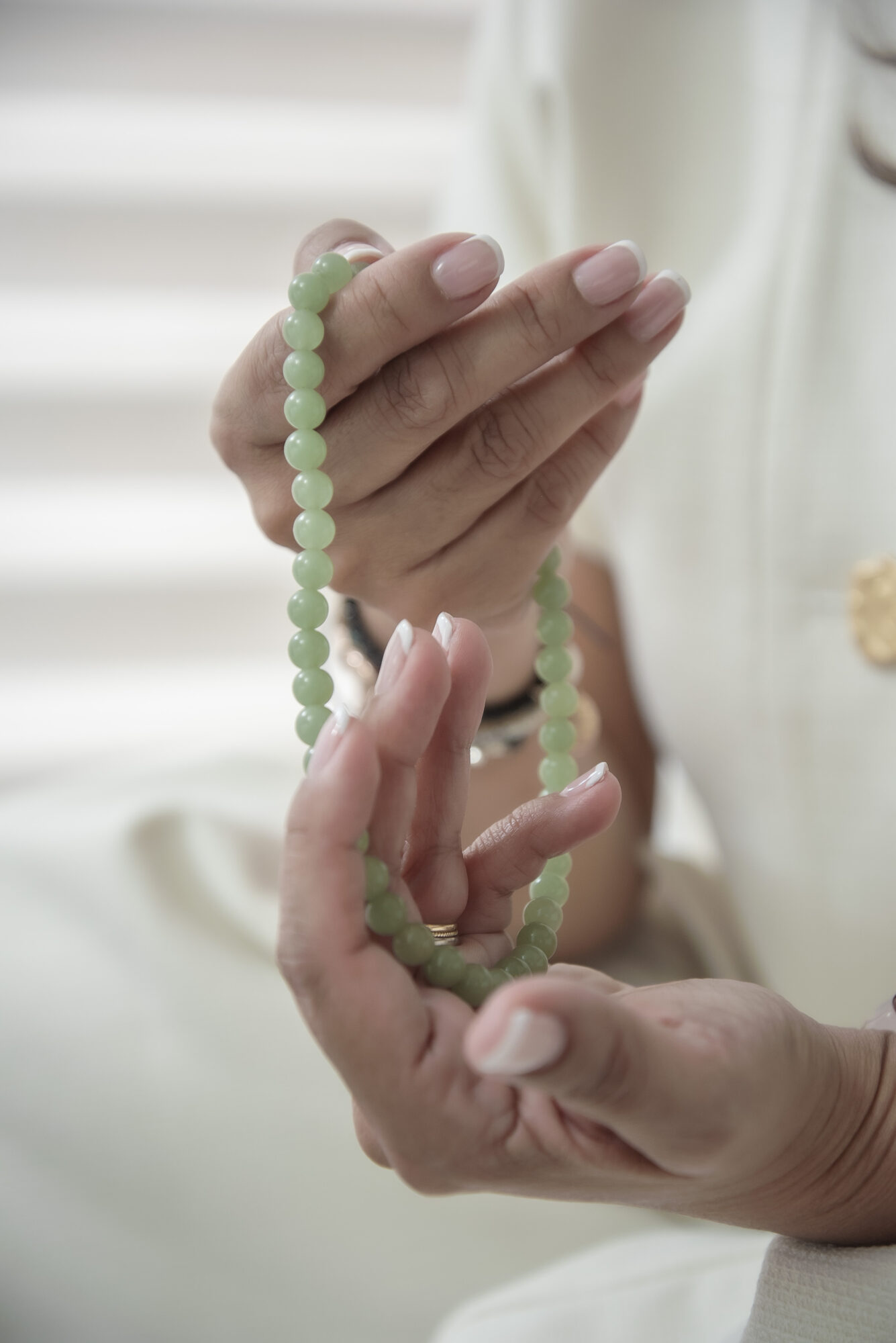 Person holding a green beaded bracelet with both hands, fingers gently grasping the beads.